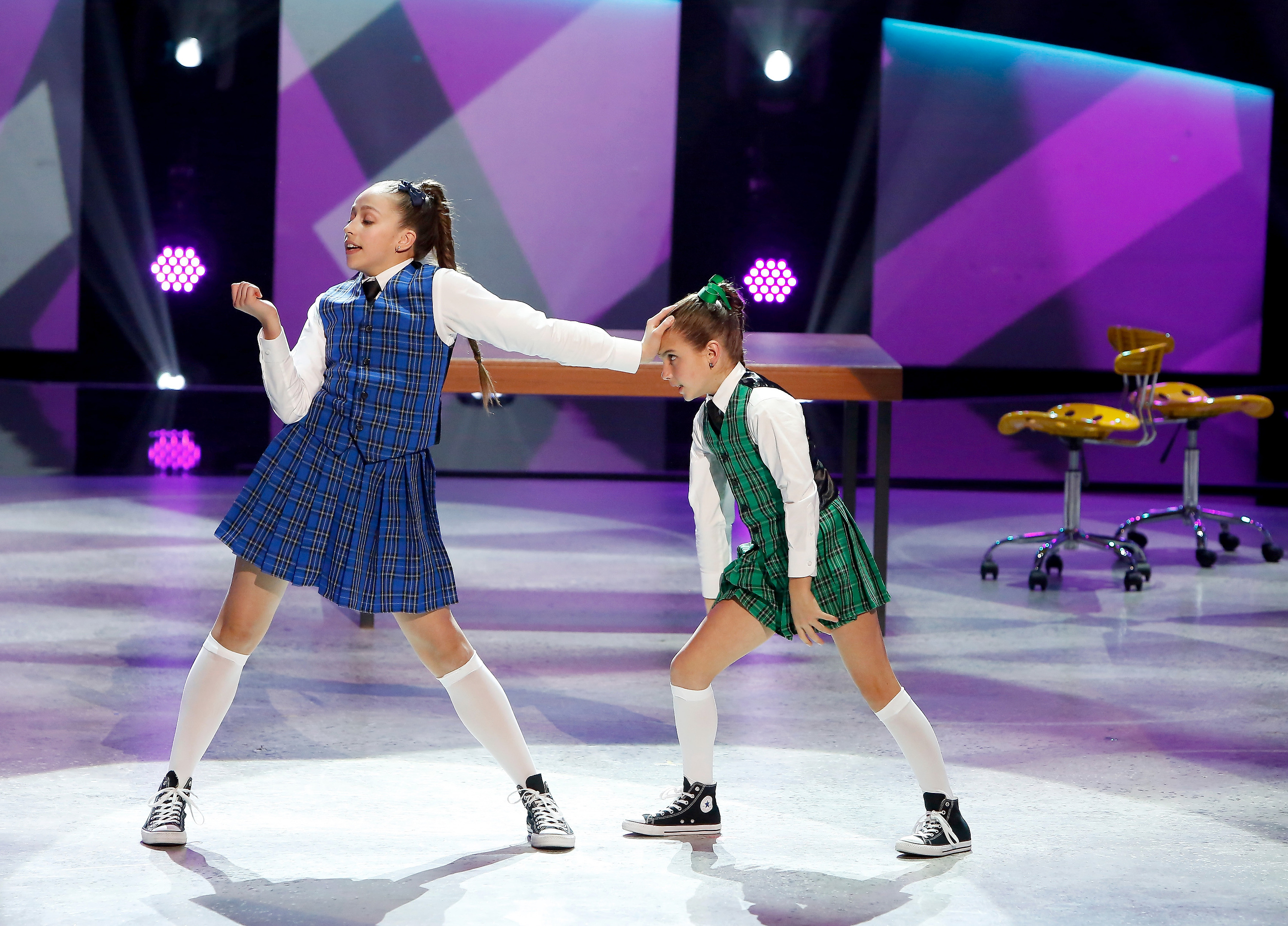 A young Tate McRae wears a school girl outfit and converse sneakers, dancing alongside another young girl in a matching outfit.