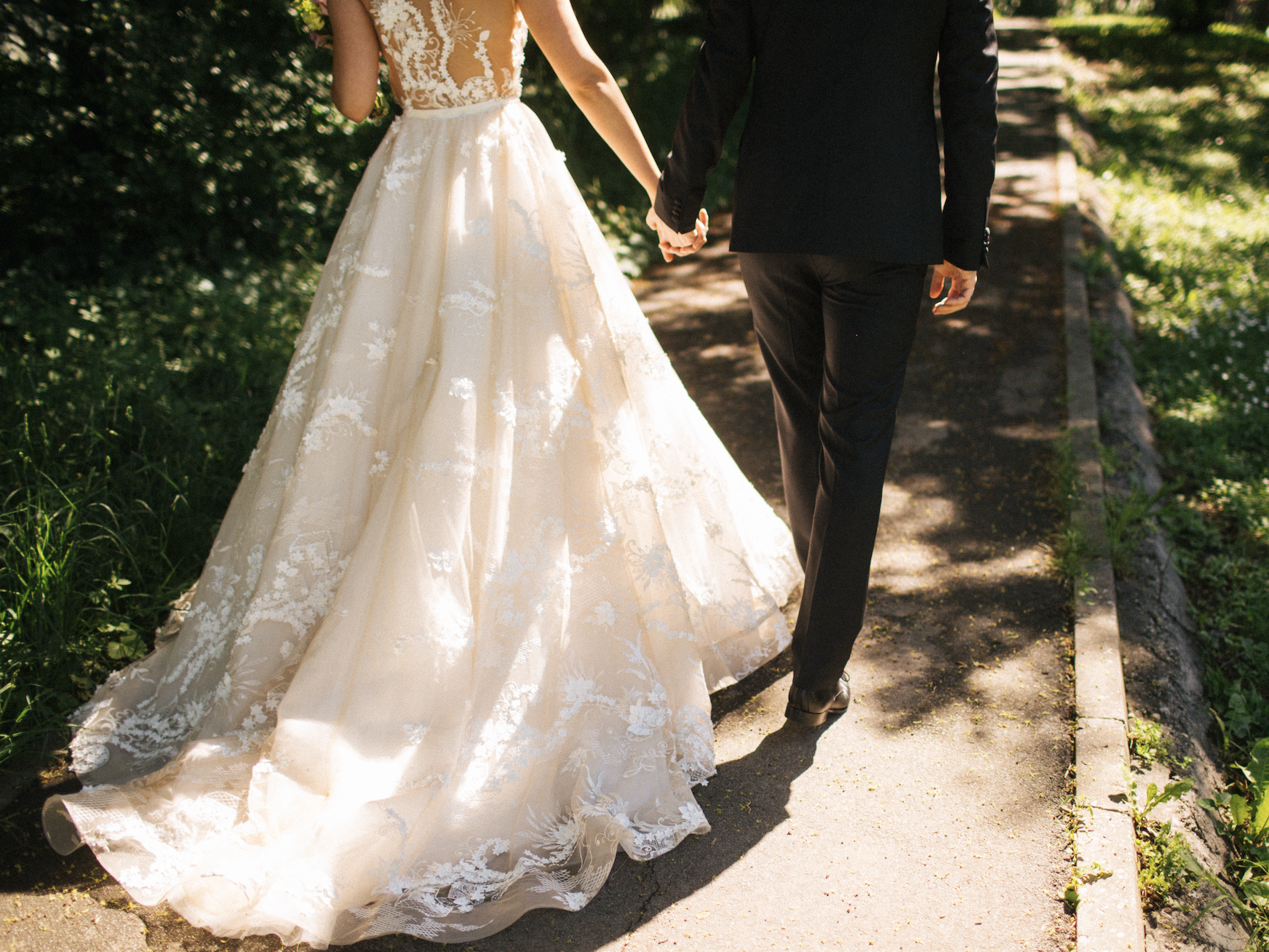 A bride and groom seen from the back on a pathway holding hands