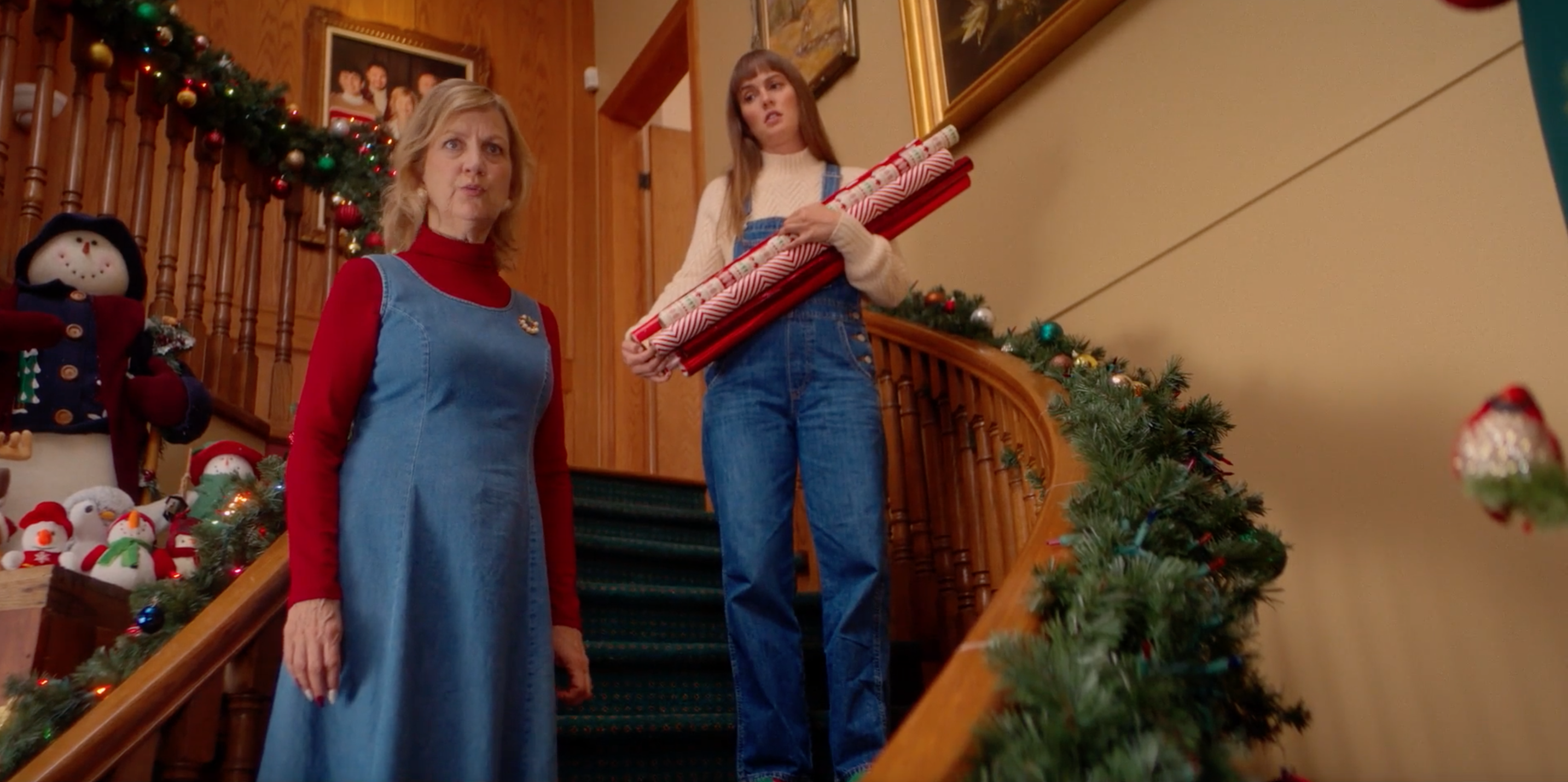 mom on the stairs defending ali who holds christmas wrapping paper. house is very decorated