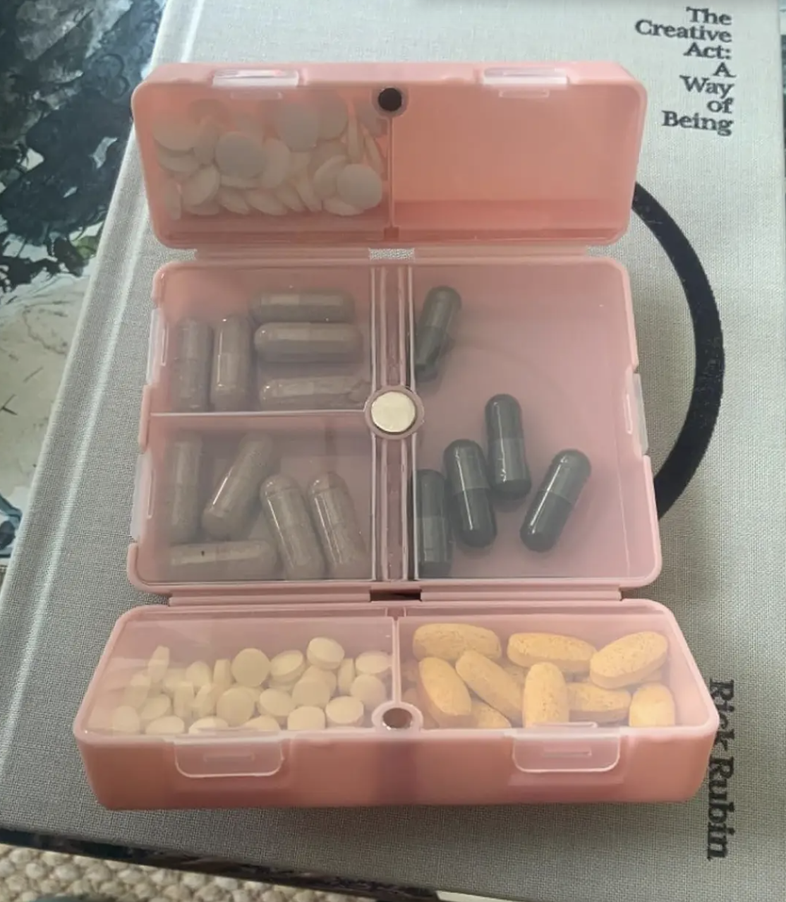 A pink folding organizer open to show capsules inside of the clear-paneled compartments