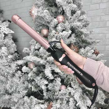 model holding pink and black curling iron in front of a Christmas tree