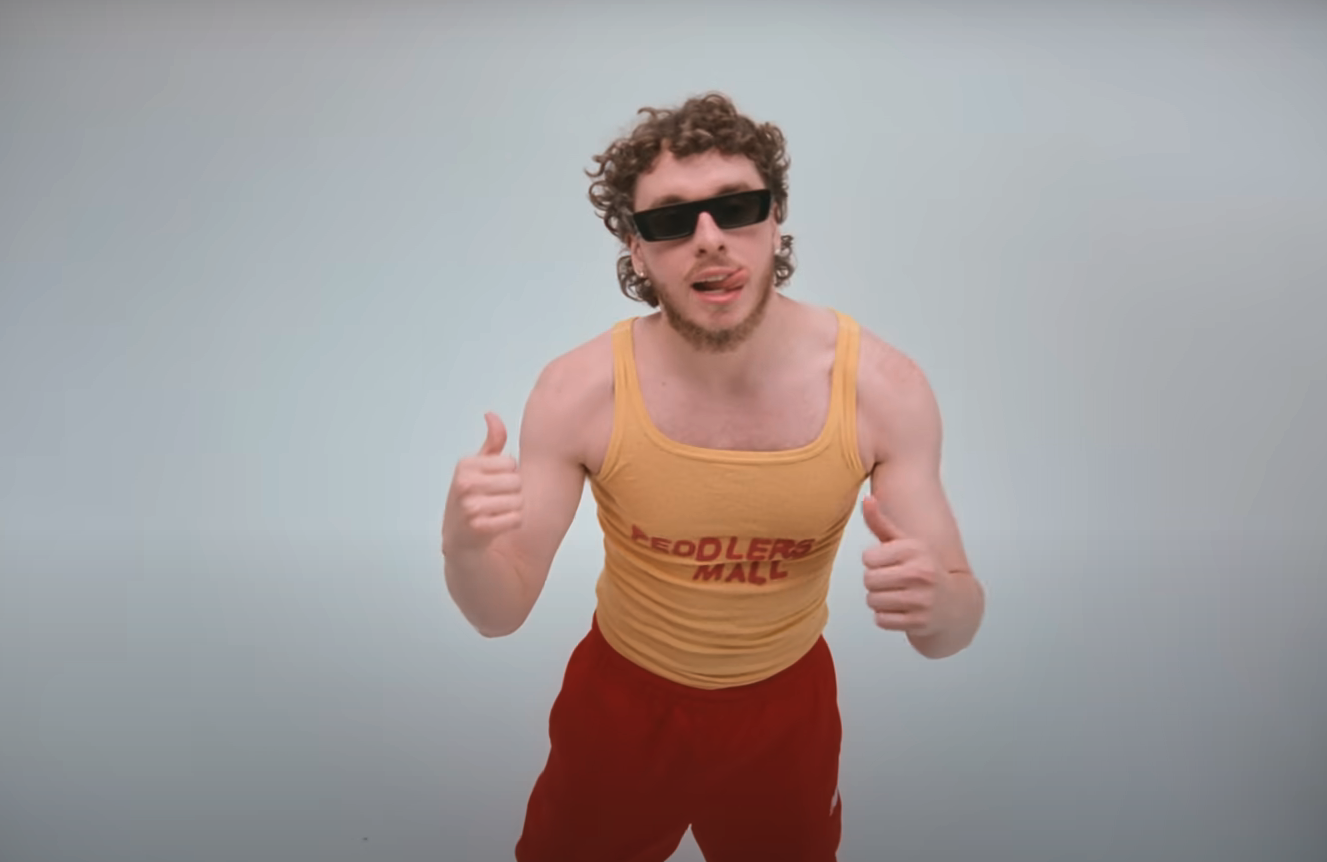 jack in the music video with a muscle tank and bright pants and sunglasses against a bare wall