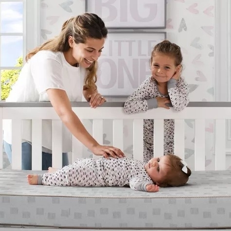A parent and child interact with a baby on a crib mattress