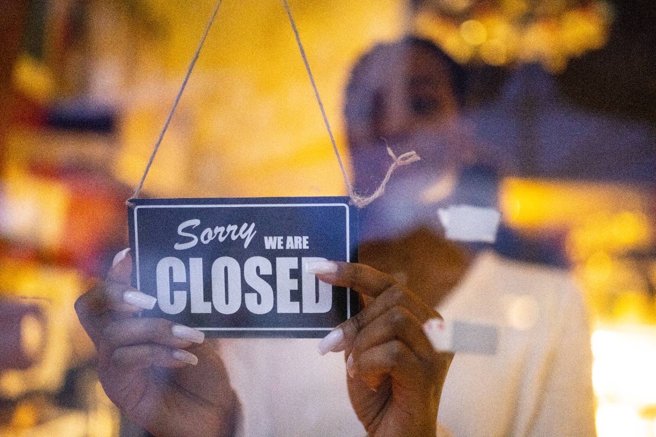 A person placing a sign that says, &quot;Sorry we are closed&quot; on a door
