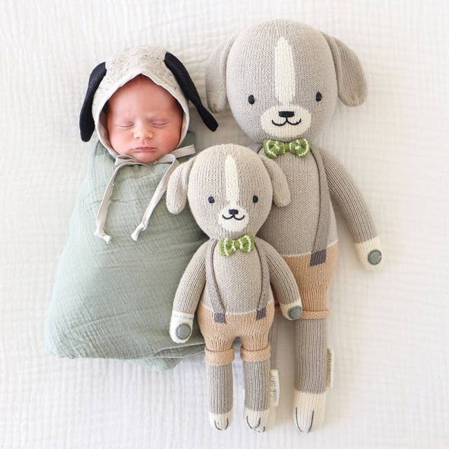 two plush hand knit dog dolls next to a newborn