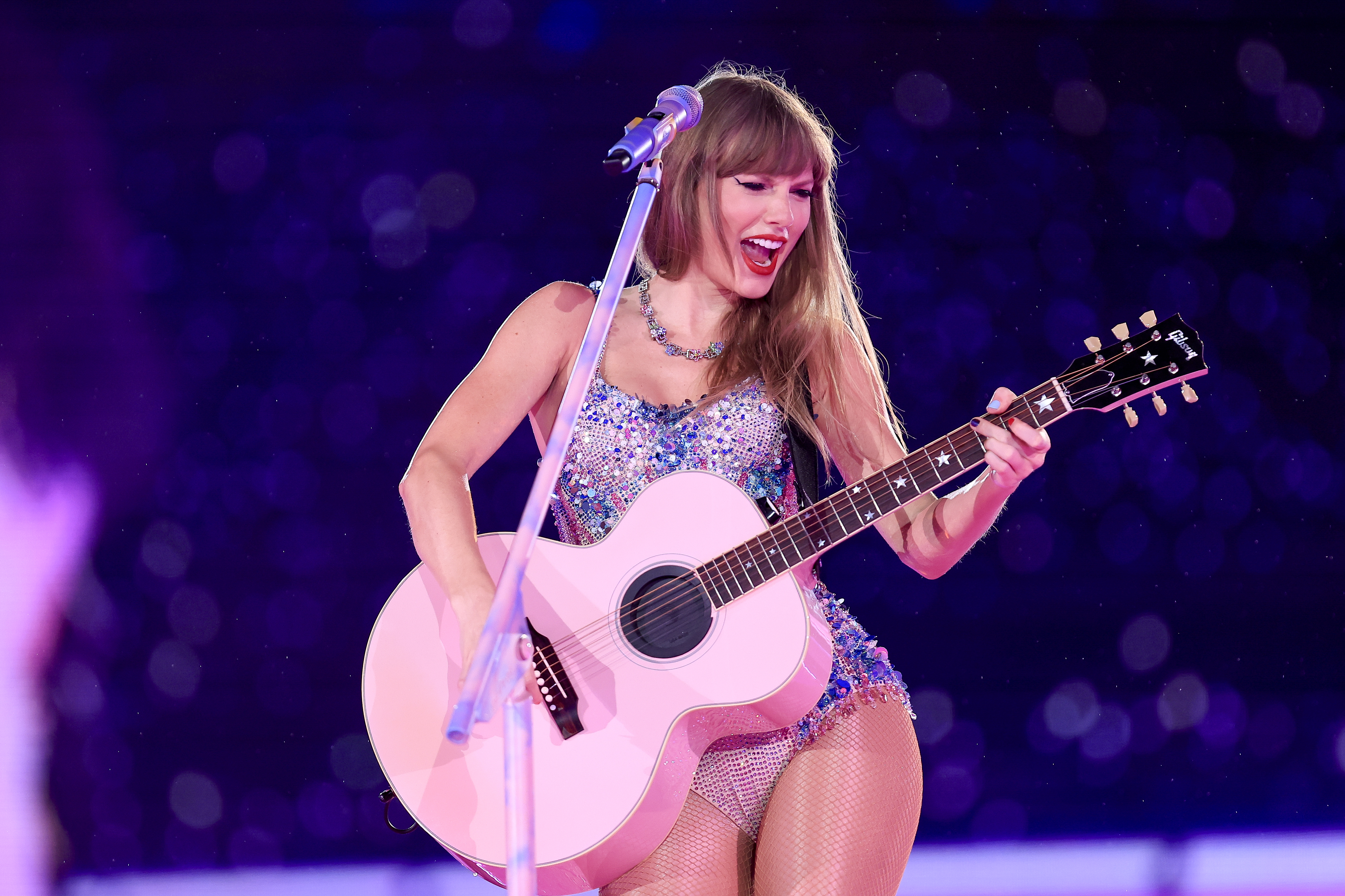 Taylor Swift onstage smiling and playing the guitar