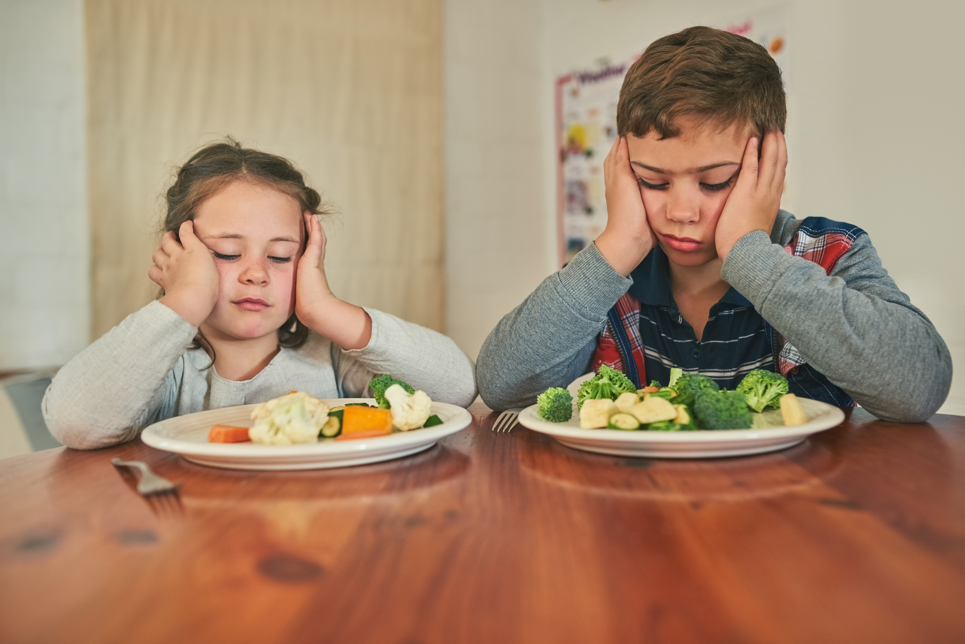 A little girl and boy looking disappointed at their plates with vegetables