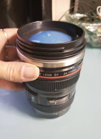 A lens shaped thermos in a reviewer's hand