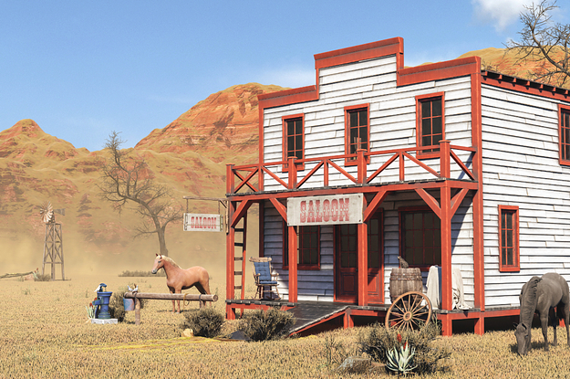 A saloon with horses grazing in front of it.