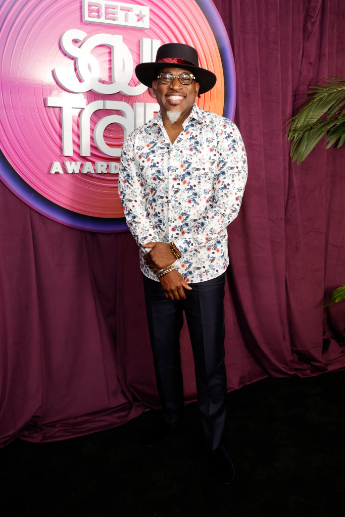 David Banner is wearing a floral-print dress shirt and slacks, as well as a fedora