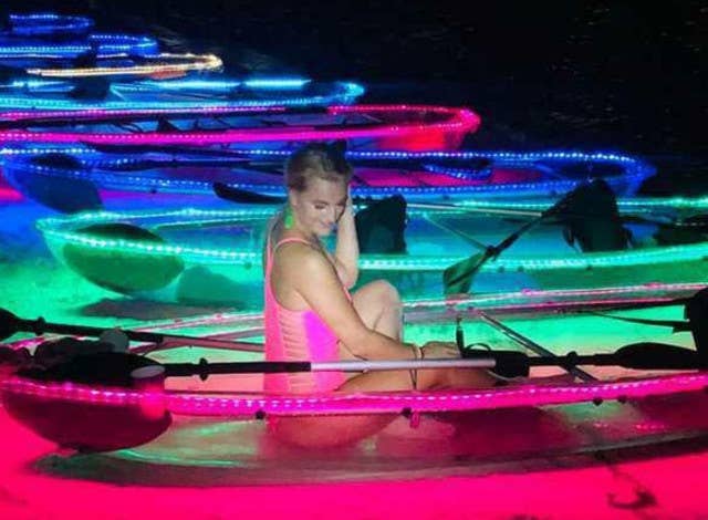 Woman sits in a neon-lit clear kayak