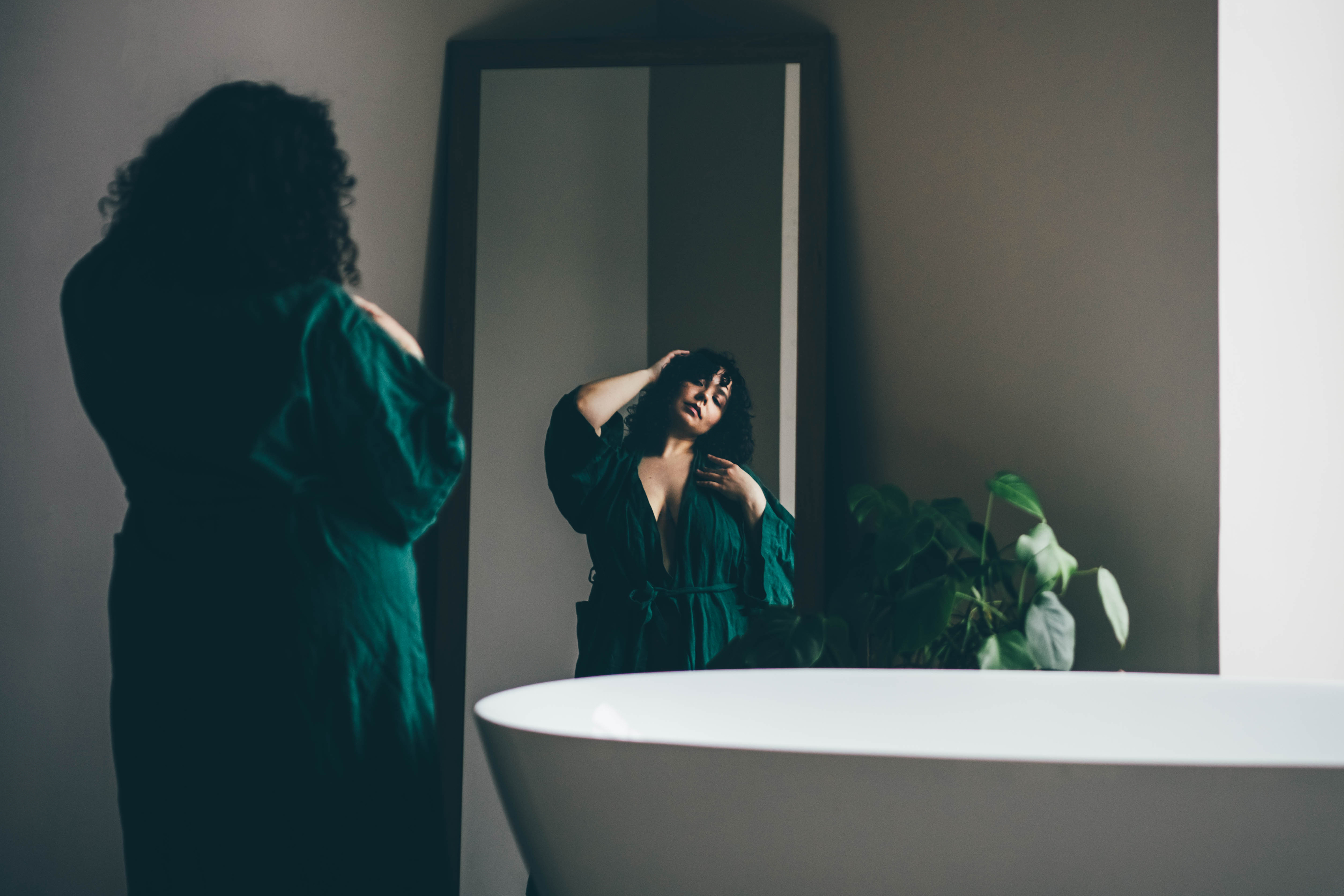 a woman in a bathroom and in her bathrobe confidently looking in the mirror