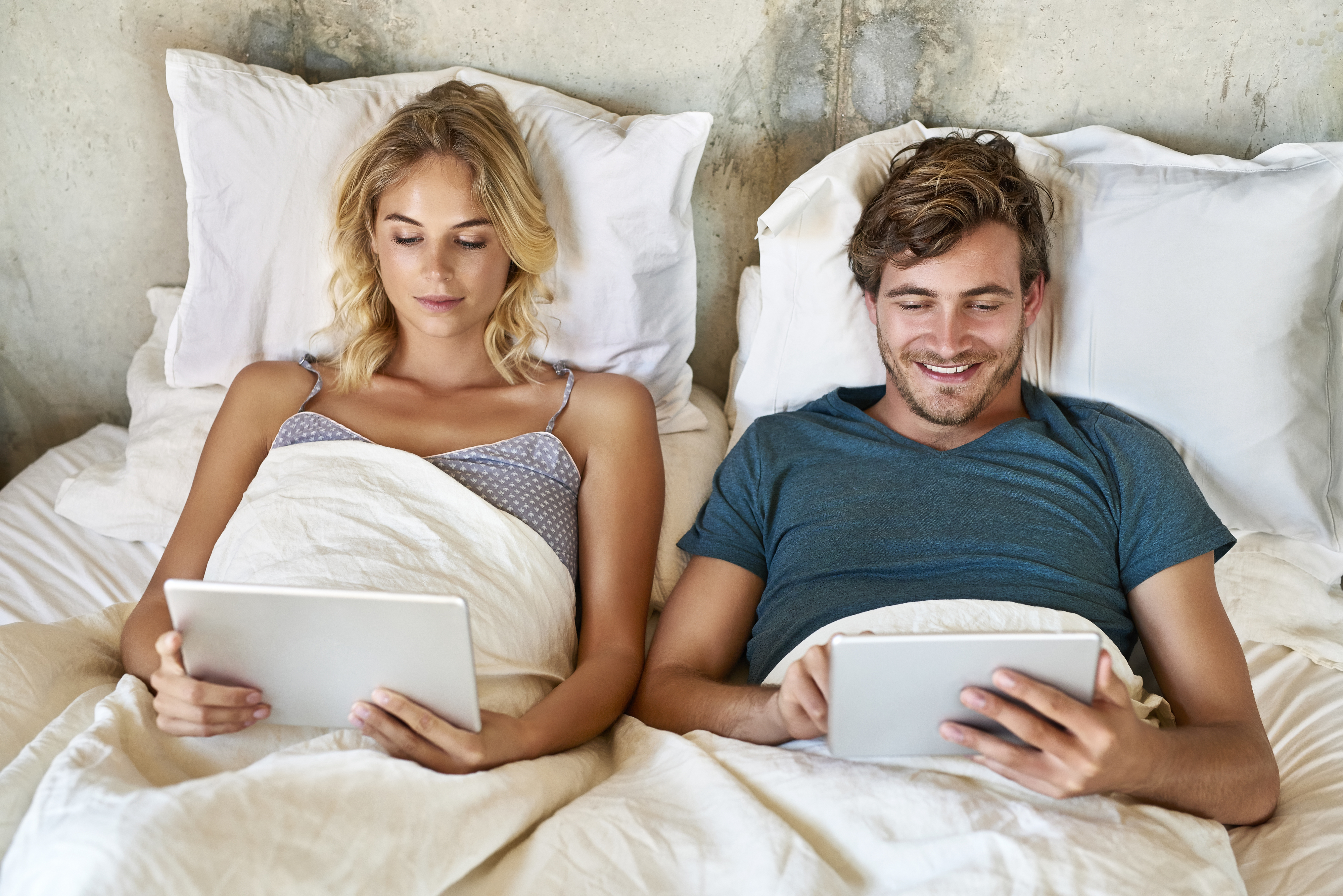 couple laying in bed while watching their tablets