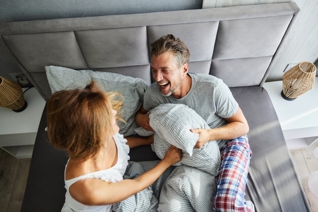 a couple in bed laughing and having a pillow fight