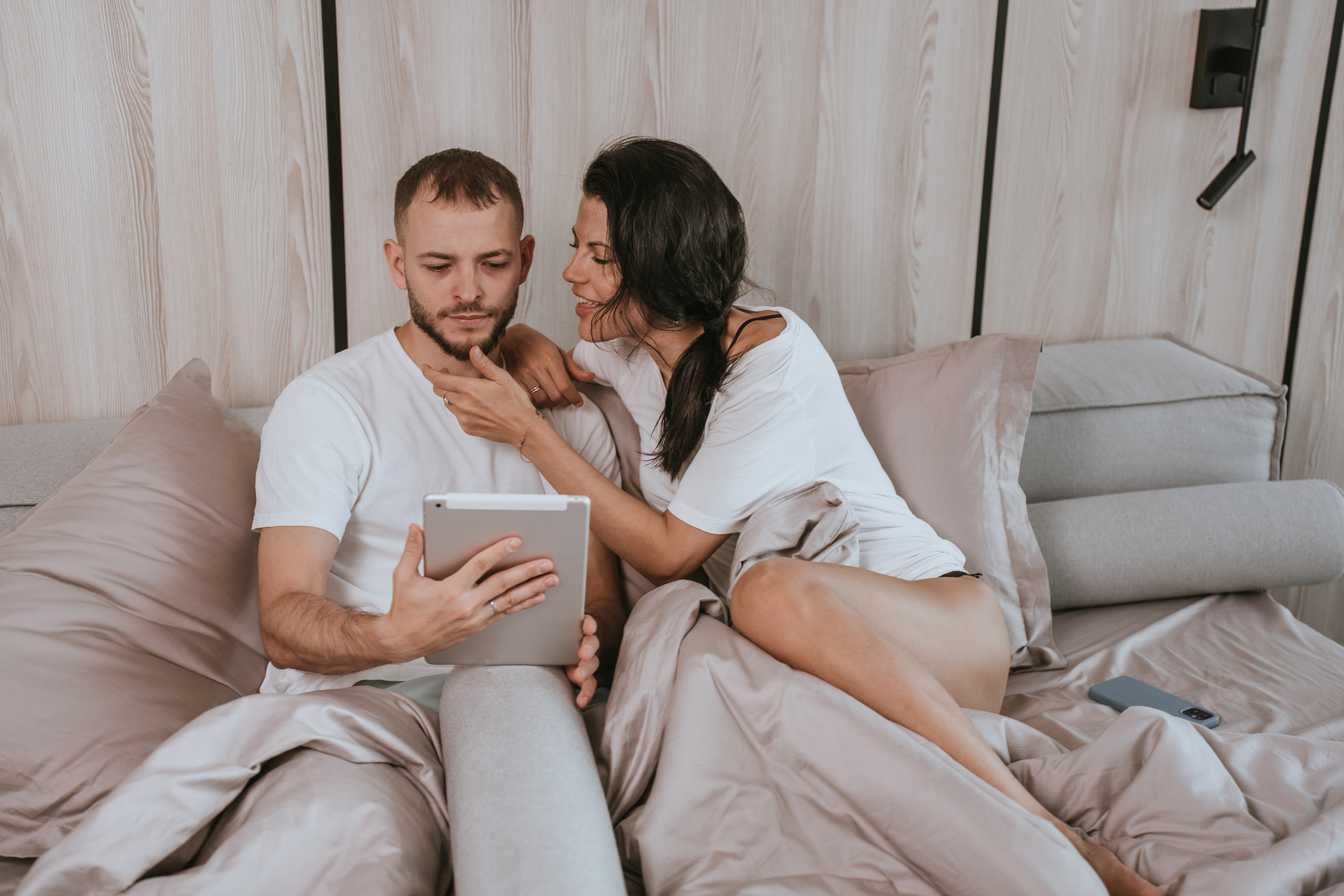 a woman trying to get her husband&#x27;s attention in bed while he stares at a tablet