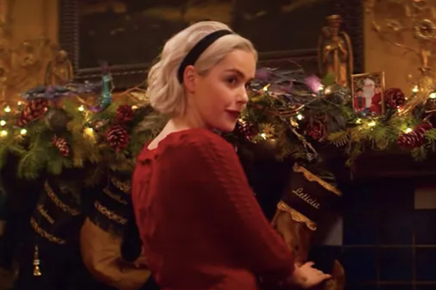 Sabrina Spellman in front of a fireplace filled with Christmas decorations.