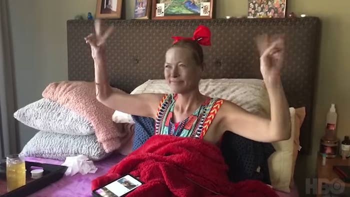 Amy Carlson making the peace sign with both her hands while sitting in bed