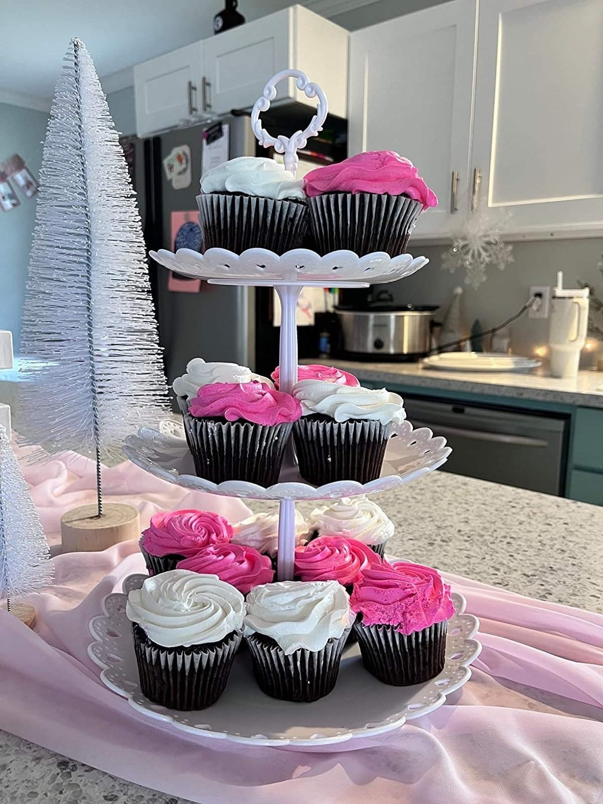 white three-tier cupcake stand with pink and white frosted chocolate cupcakes