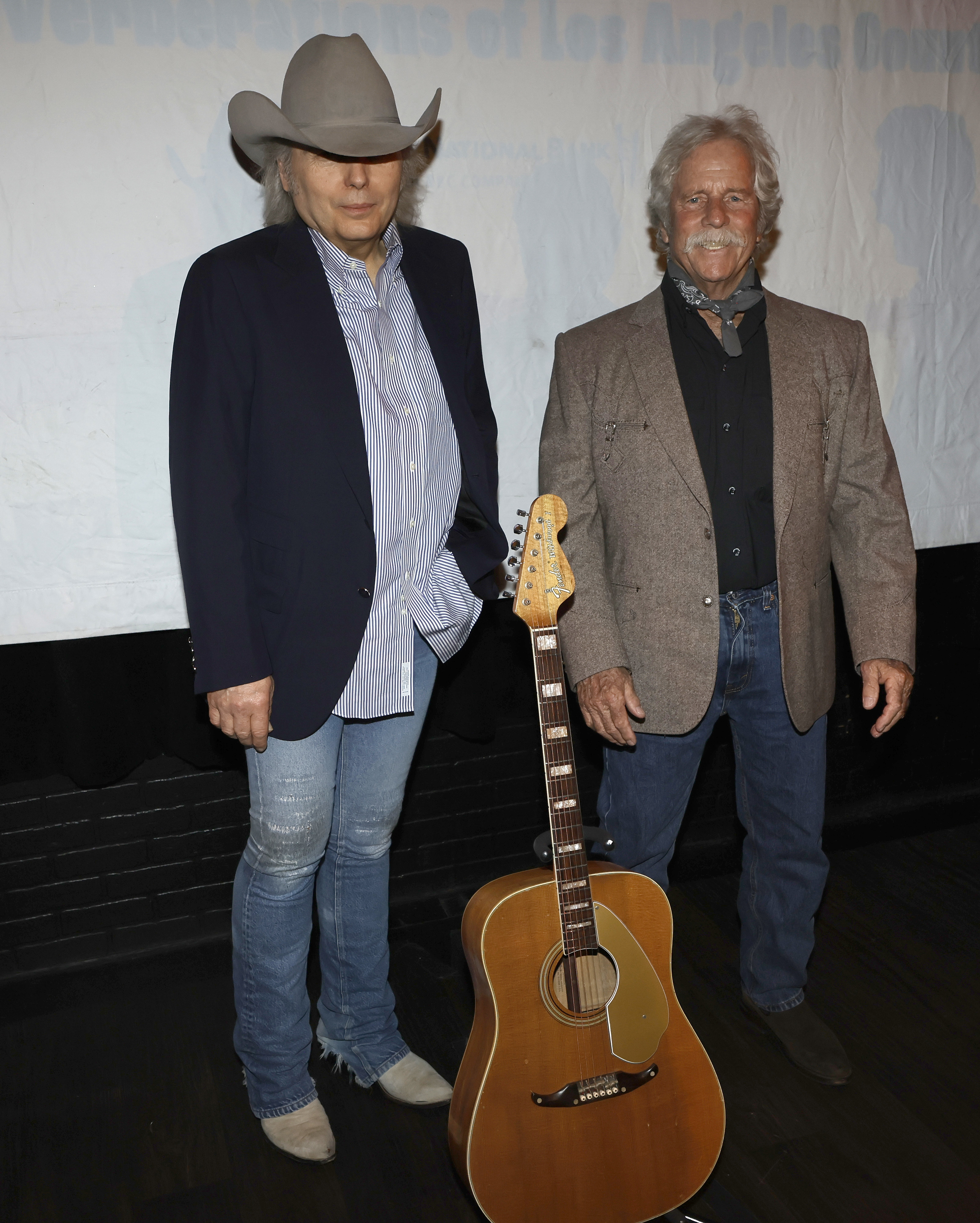 Dwight wearing a Western-style hat and jeans, with a guitar in front of him and Chris