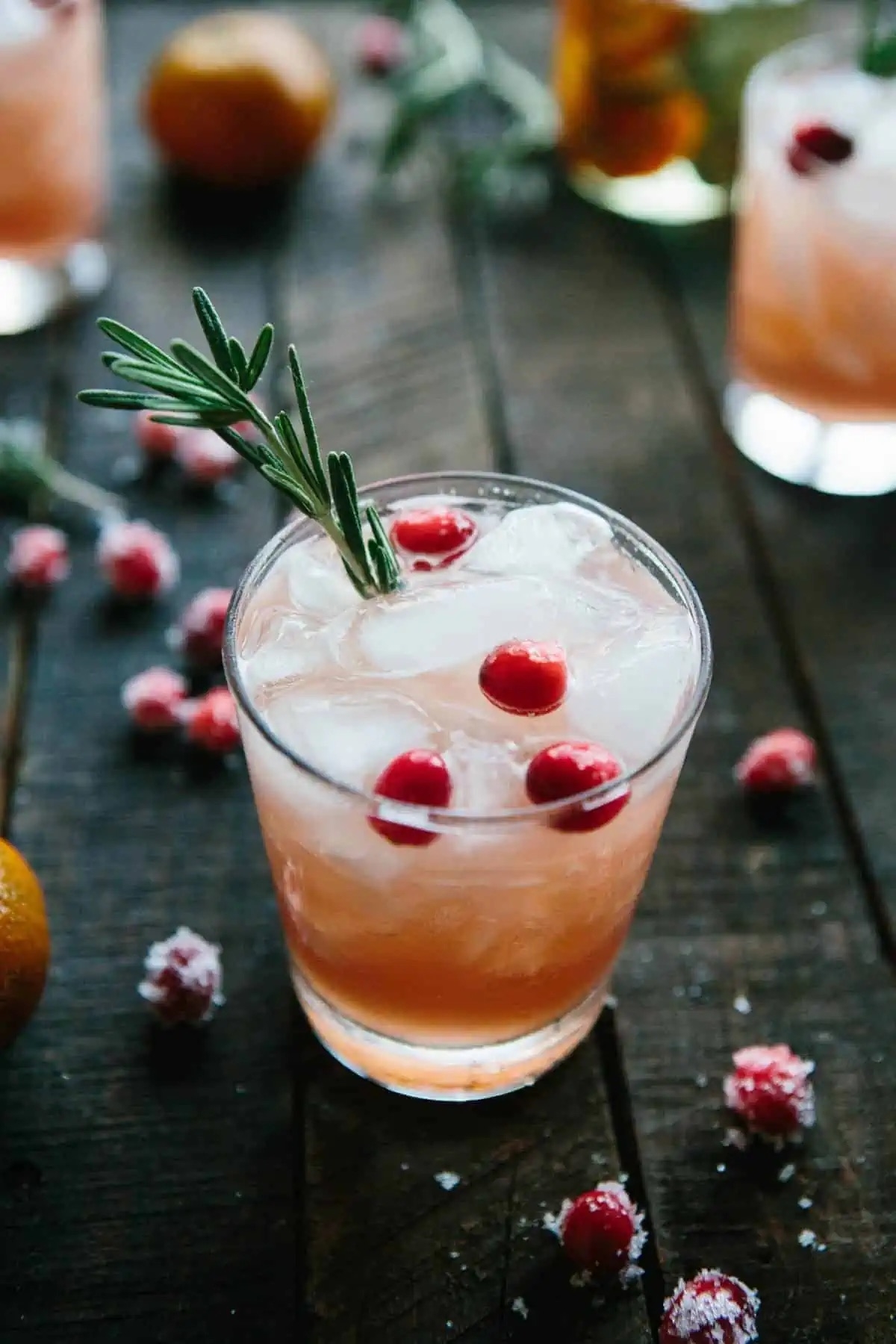 a cocktail in a glass topped with fresh cranberries and sprig of rosemary