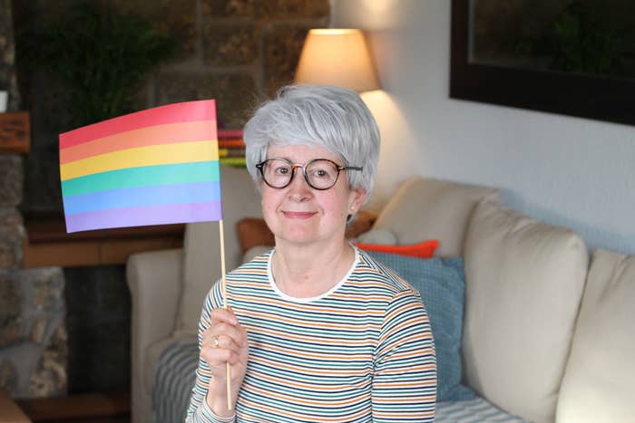 older woman sitting on a couch and holding up a pride flag