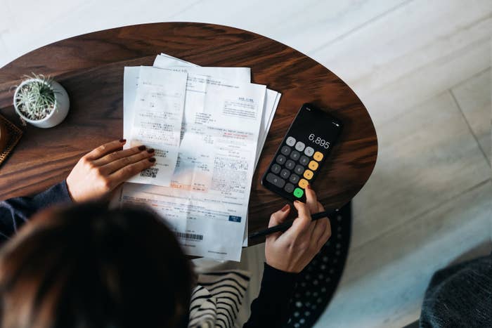 woman with calculator and financial paperwork sits at a wood table