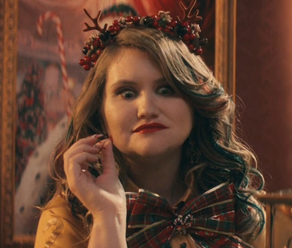 Close-up of a woman wearing a holiday wreath crown and bow and looking shocked