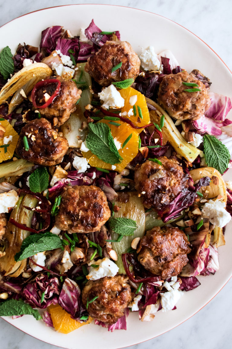 Meatballs plated on top a bed of vegetables and feta