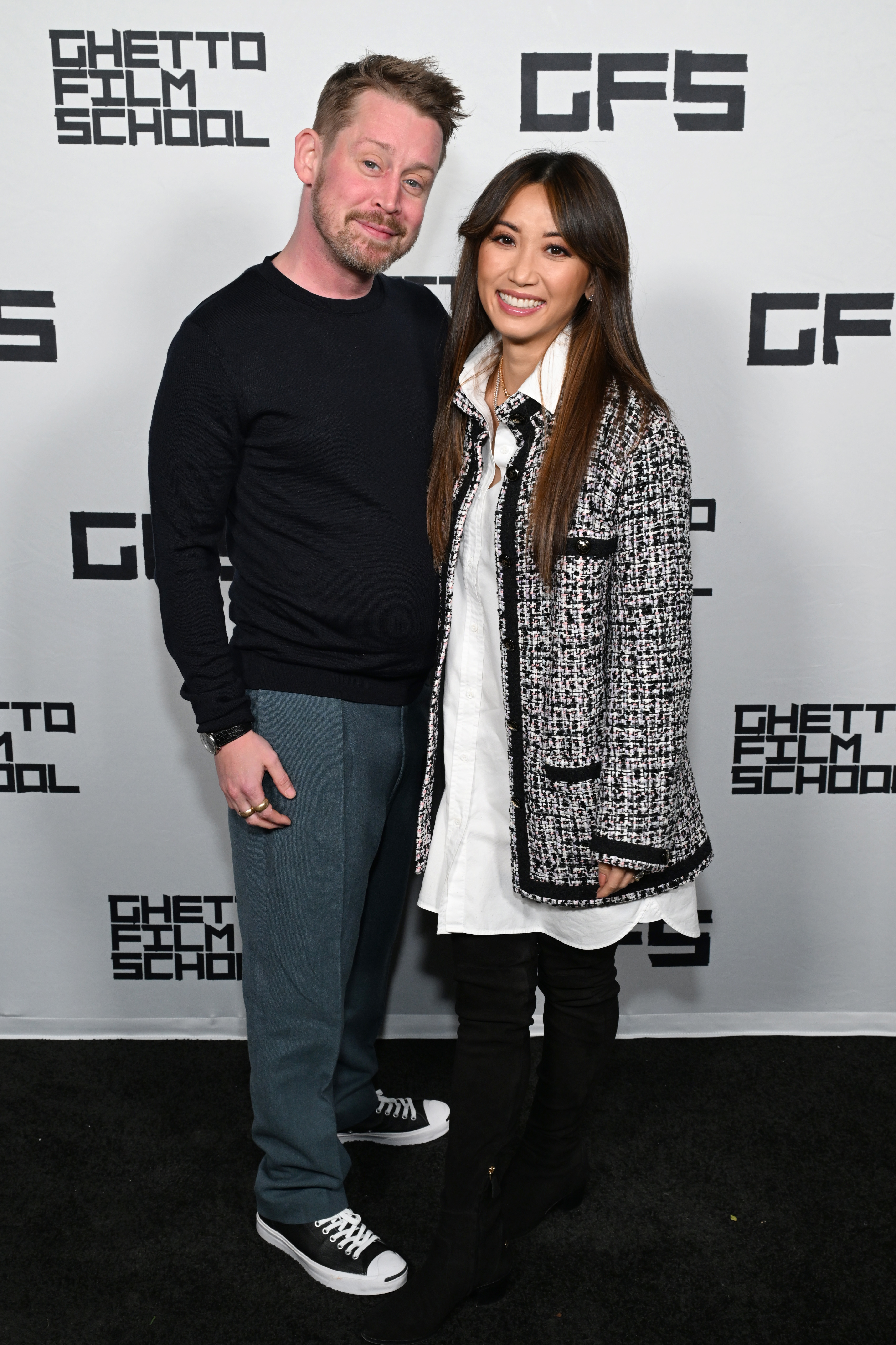 Close-up of Macaulay in a top, pants, and sneakers at a media event with Brenda Song