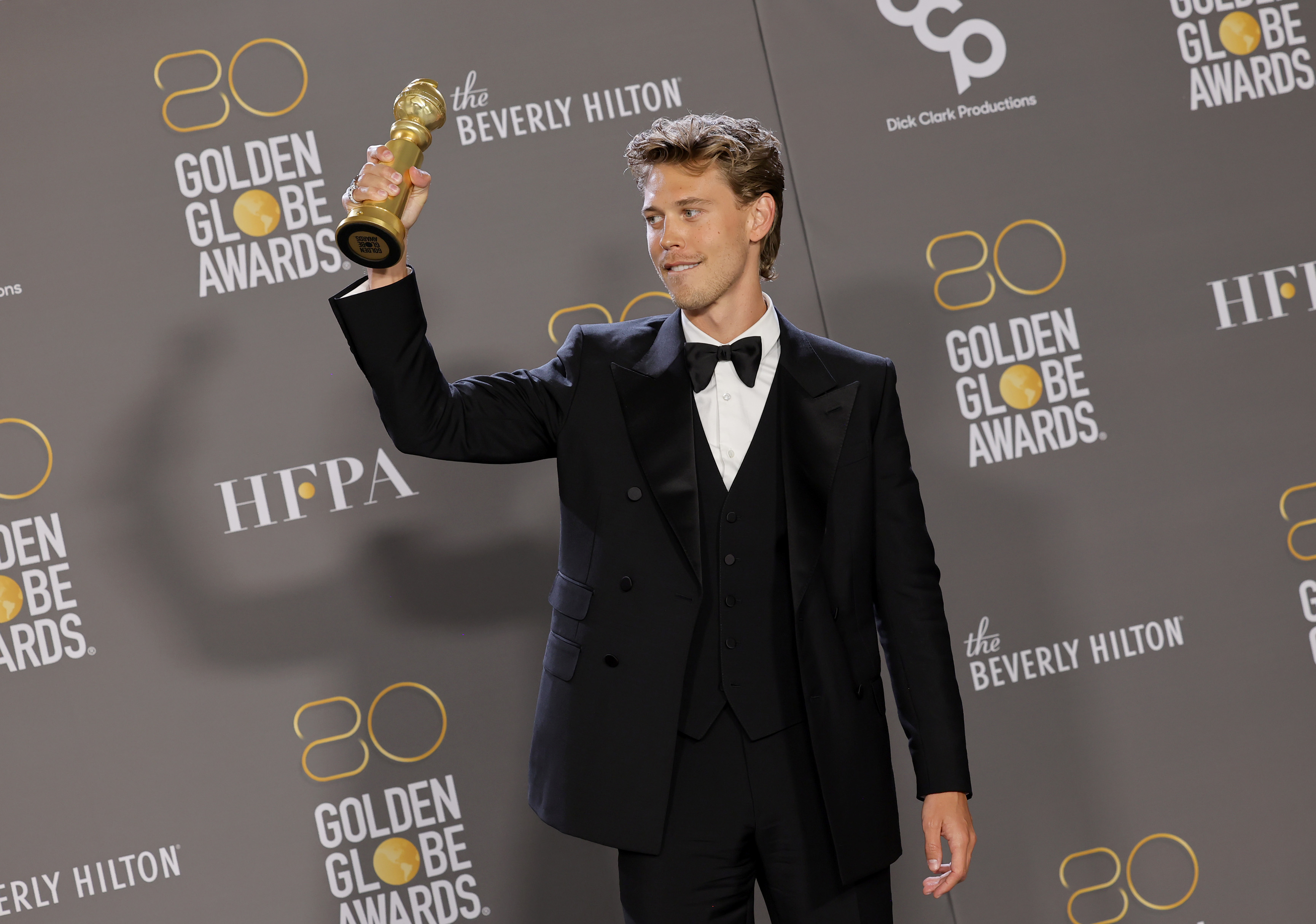 Close-up of Austin in a suit and bow tie holding up a Golden Globe