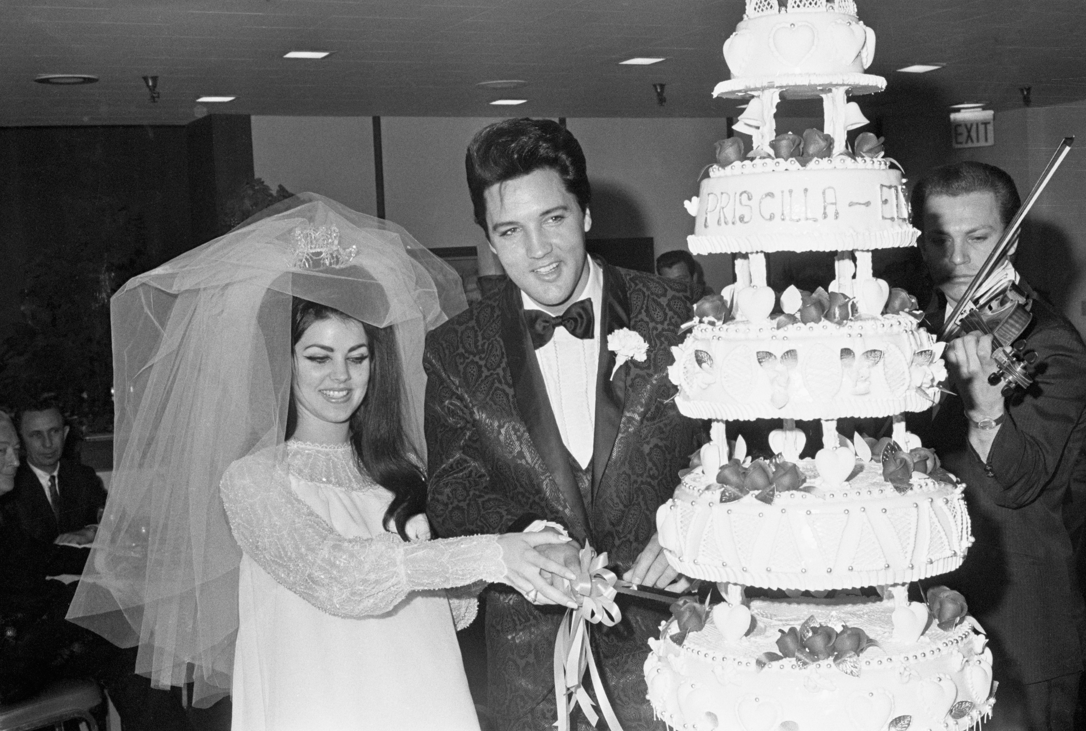 Close-up of the real Elvis and Priscilla smiling as they cut their wedding cake