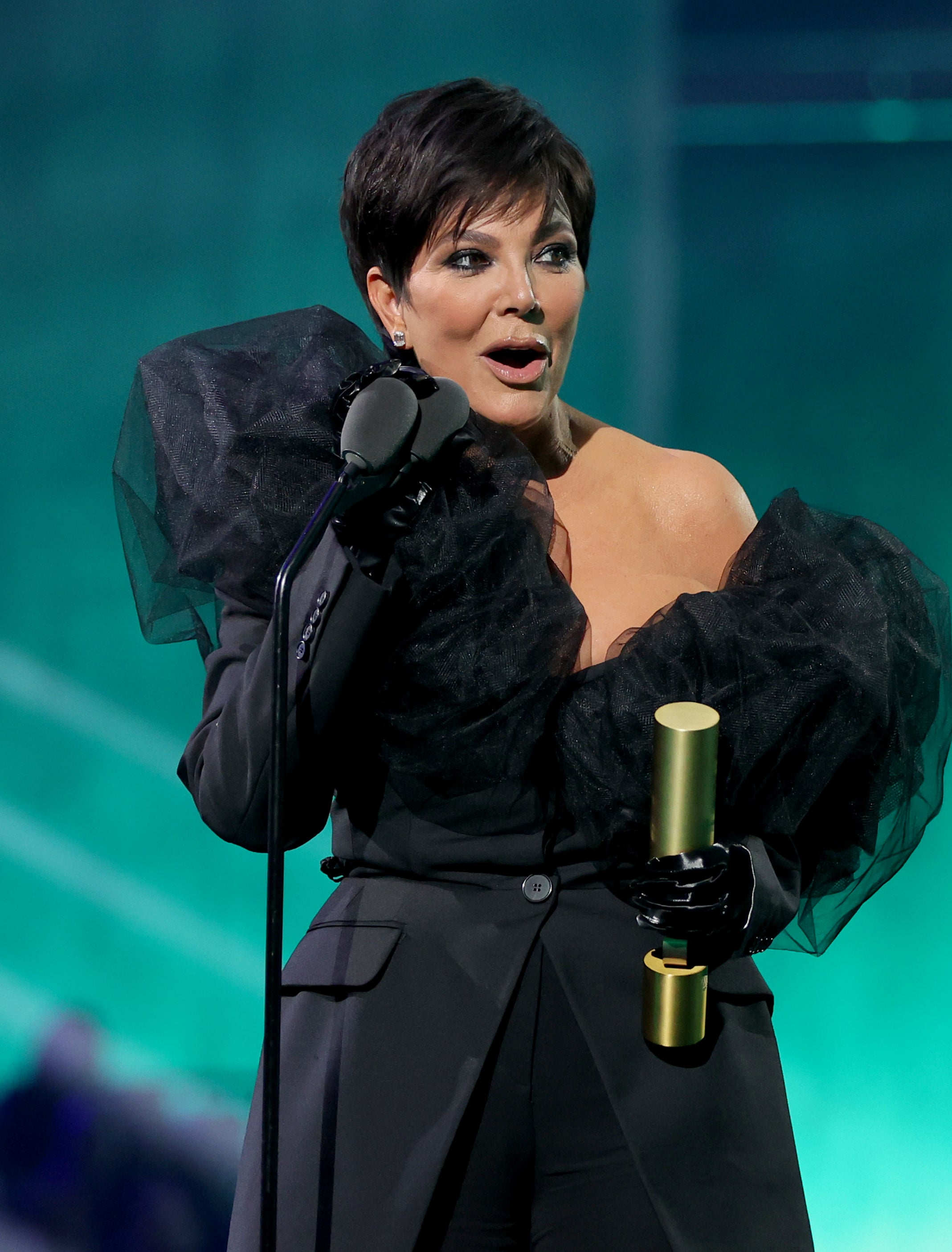 Close-up of Kris onstage at a microphone holding an award