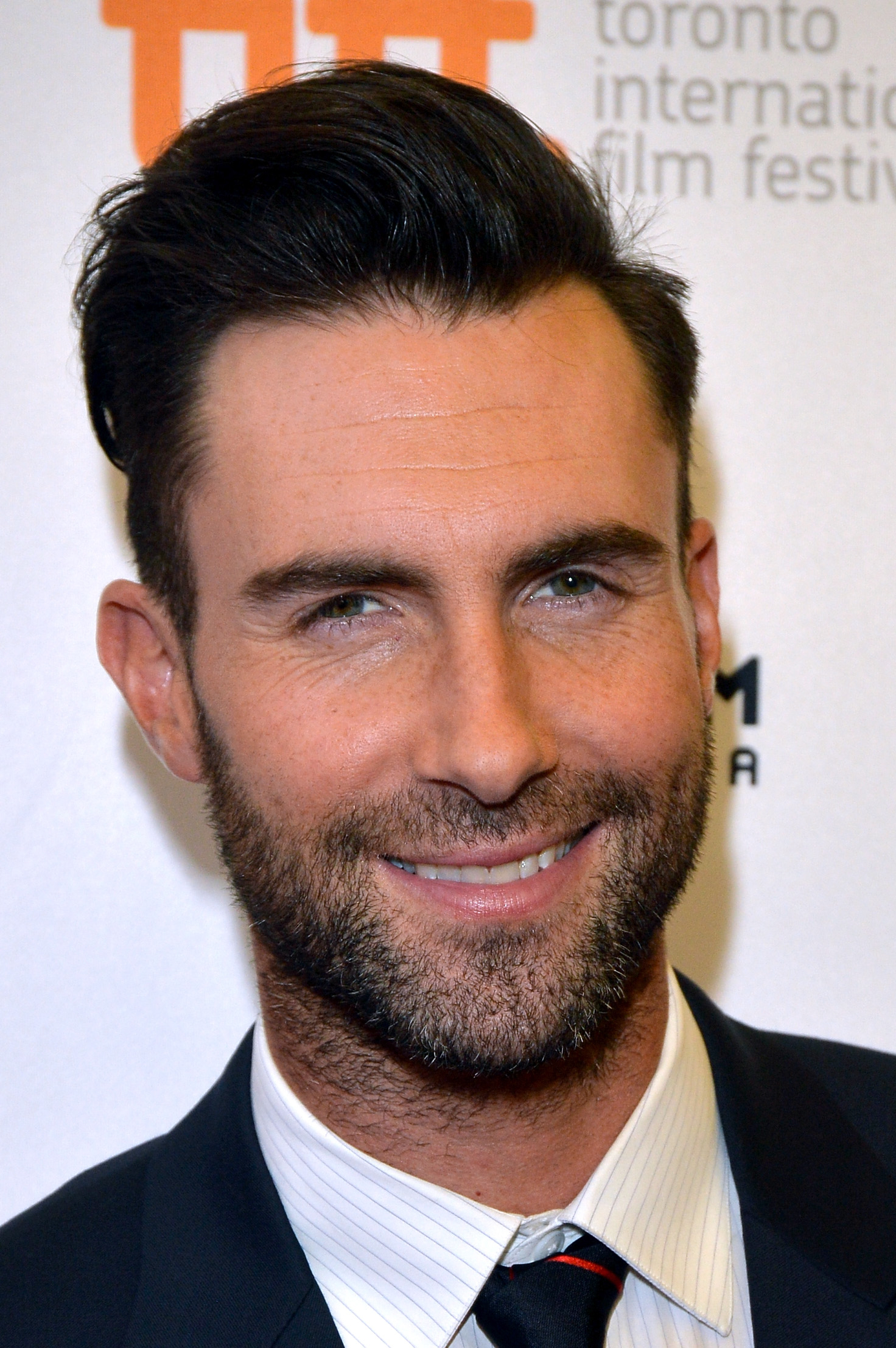 Close-up of Adam smiling in a suit and tie at a media event