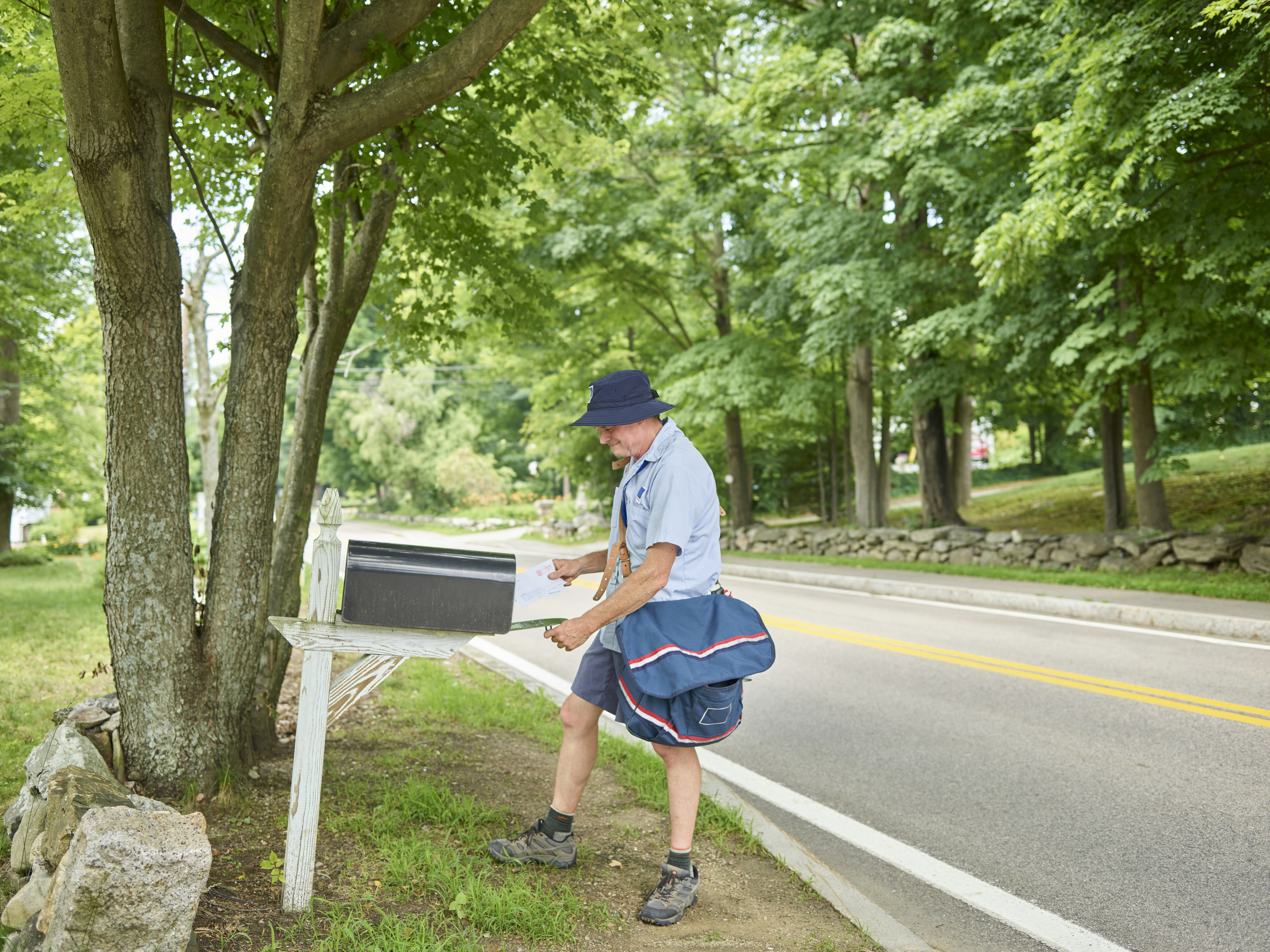 carrier putting a letter in a mailbox on a rural road