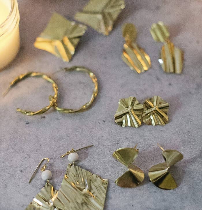 A candle illuminates a collection of textured gold earrings.