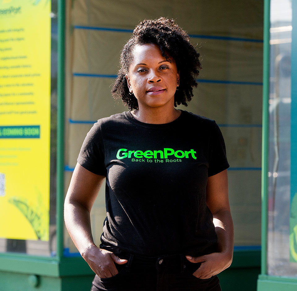 Vivianne Wilson poses in front of GreenPort store wearing a shirt that reads &quot;GreenPort: Back to the Roots.&quot;