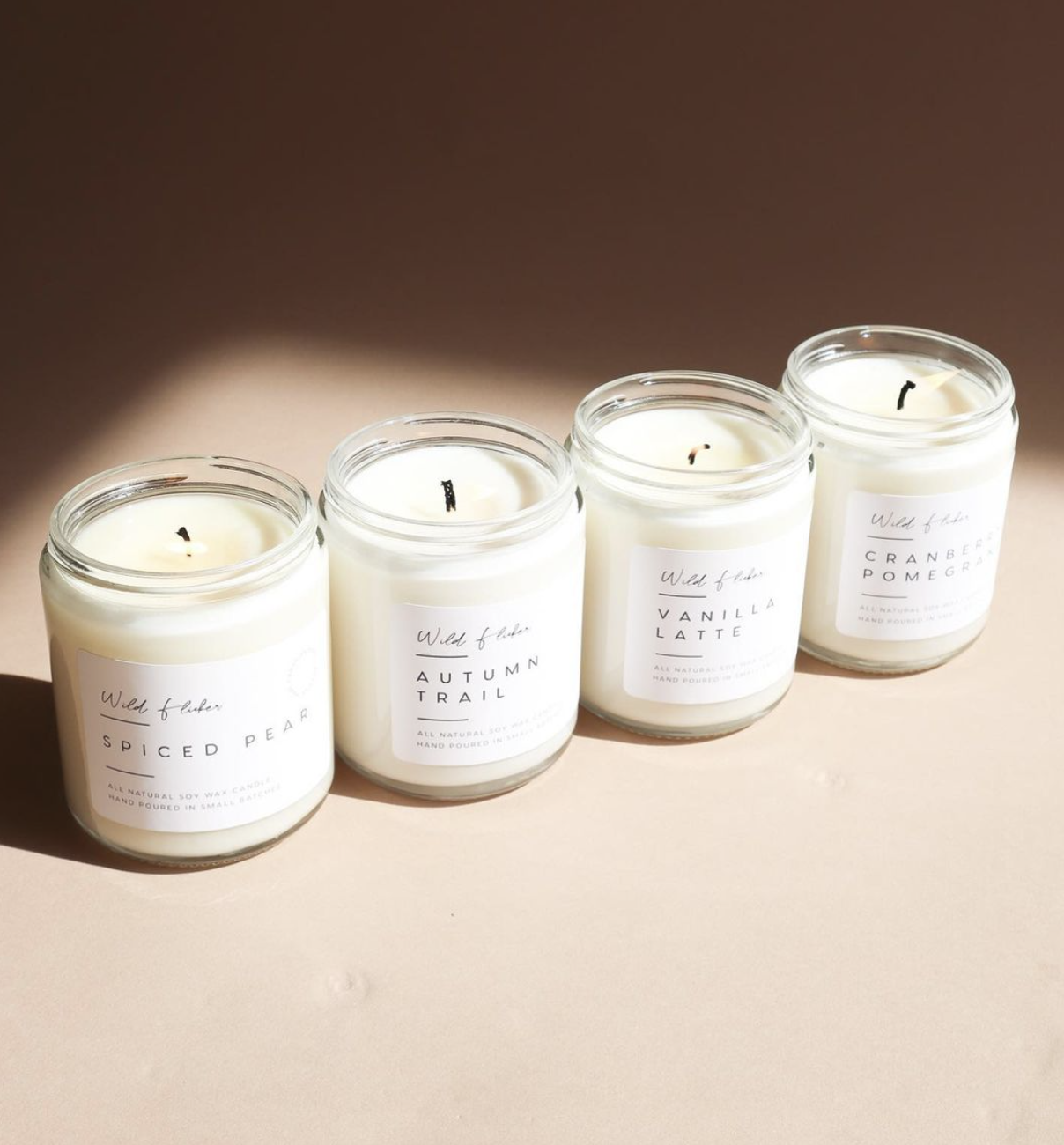 Four candles are posed on a neutral background. They have minimalist labelling which reads &quot;Wild Flicker.&quot;