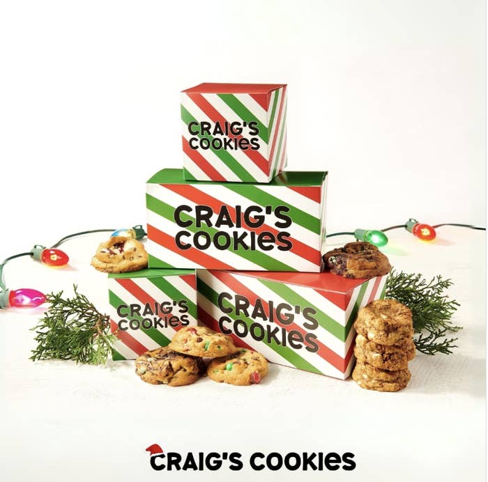 Stacks of candy-cane stripped boxes say &quot;Craig&#x27;s Cookies.&quot; Cookies are posed around the small pyramid of boxes.