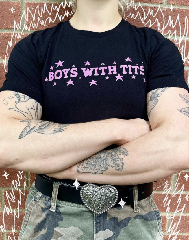 Person with tattoos crosses their arms. Tshirt reads &quot;BOYS WITH TITS&quot; with stars around it.