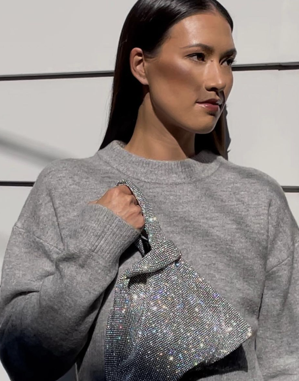 Woman wears a grey crewneck and holds a crystallized, sparkly silver purse.