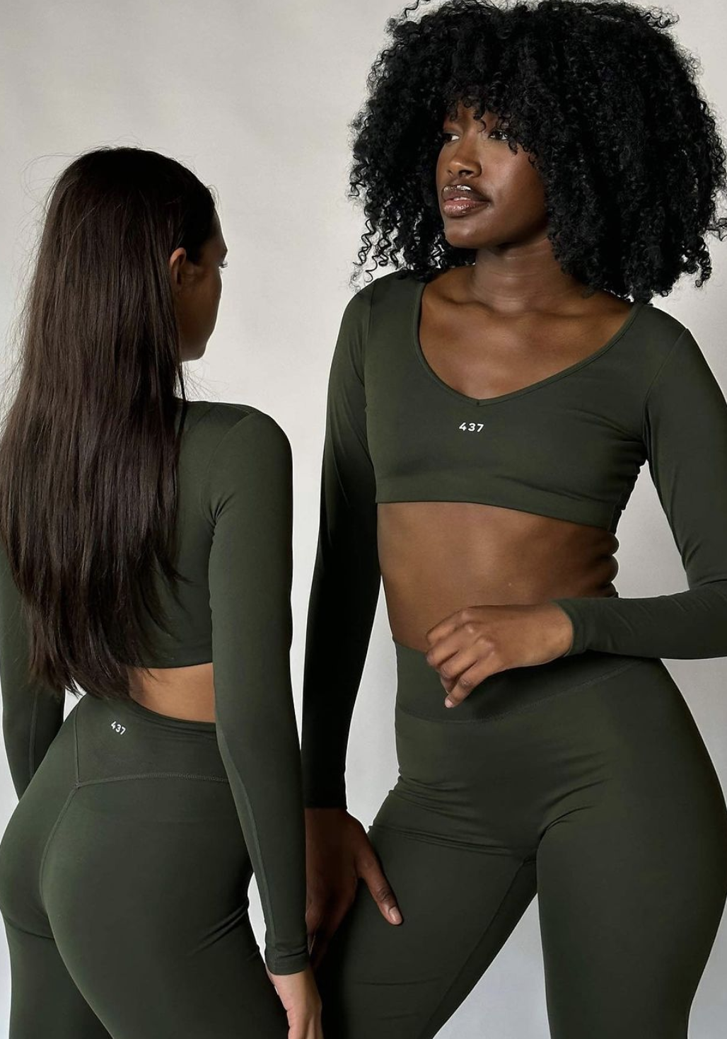 Two women pose in dark green athletic body suits that read &quot;437&quot; in small print.