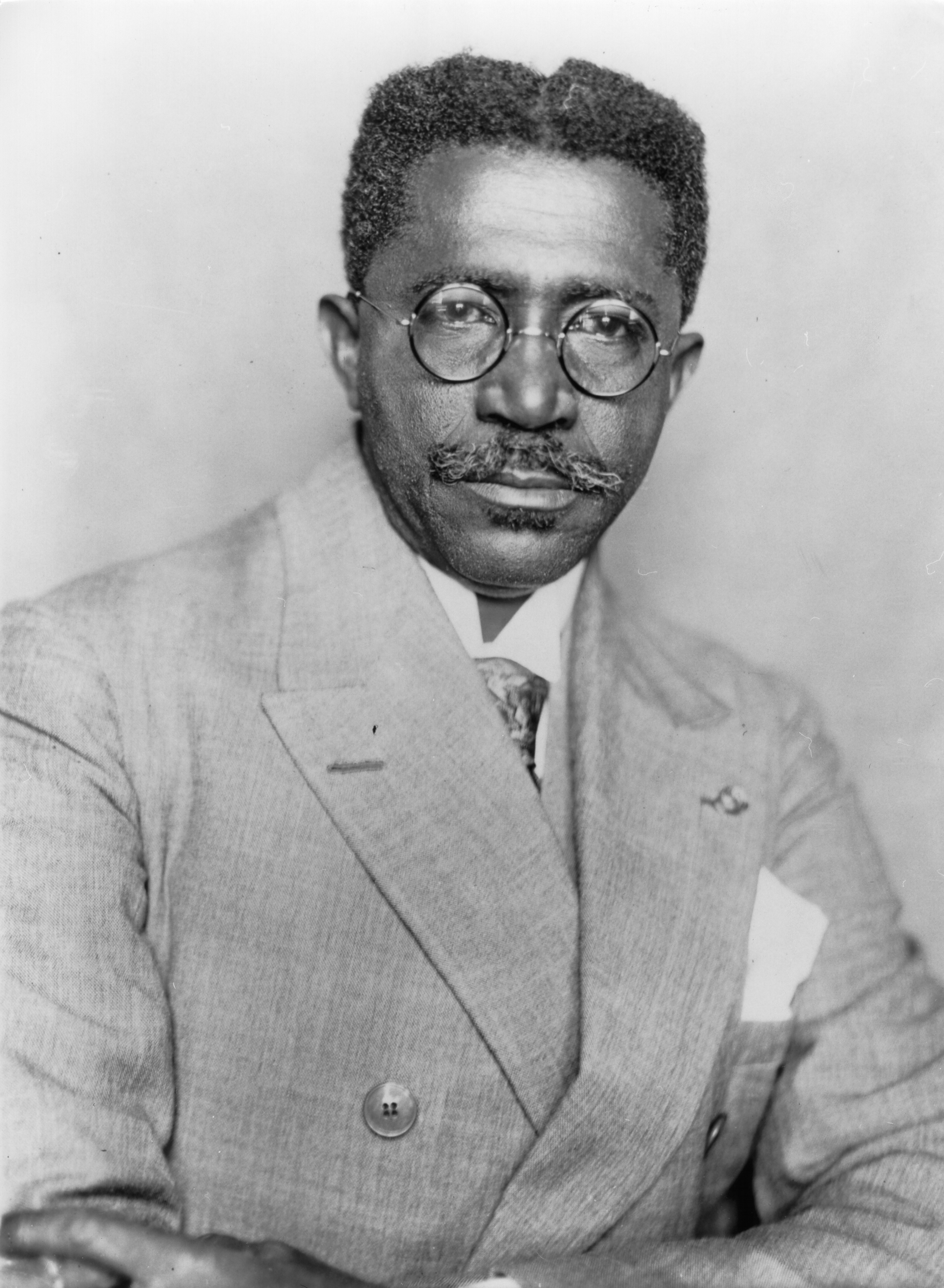 Charles D.B. King sitting for a photography portrait in a sharp linen suit and round glasses