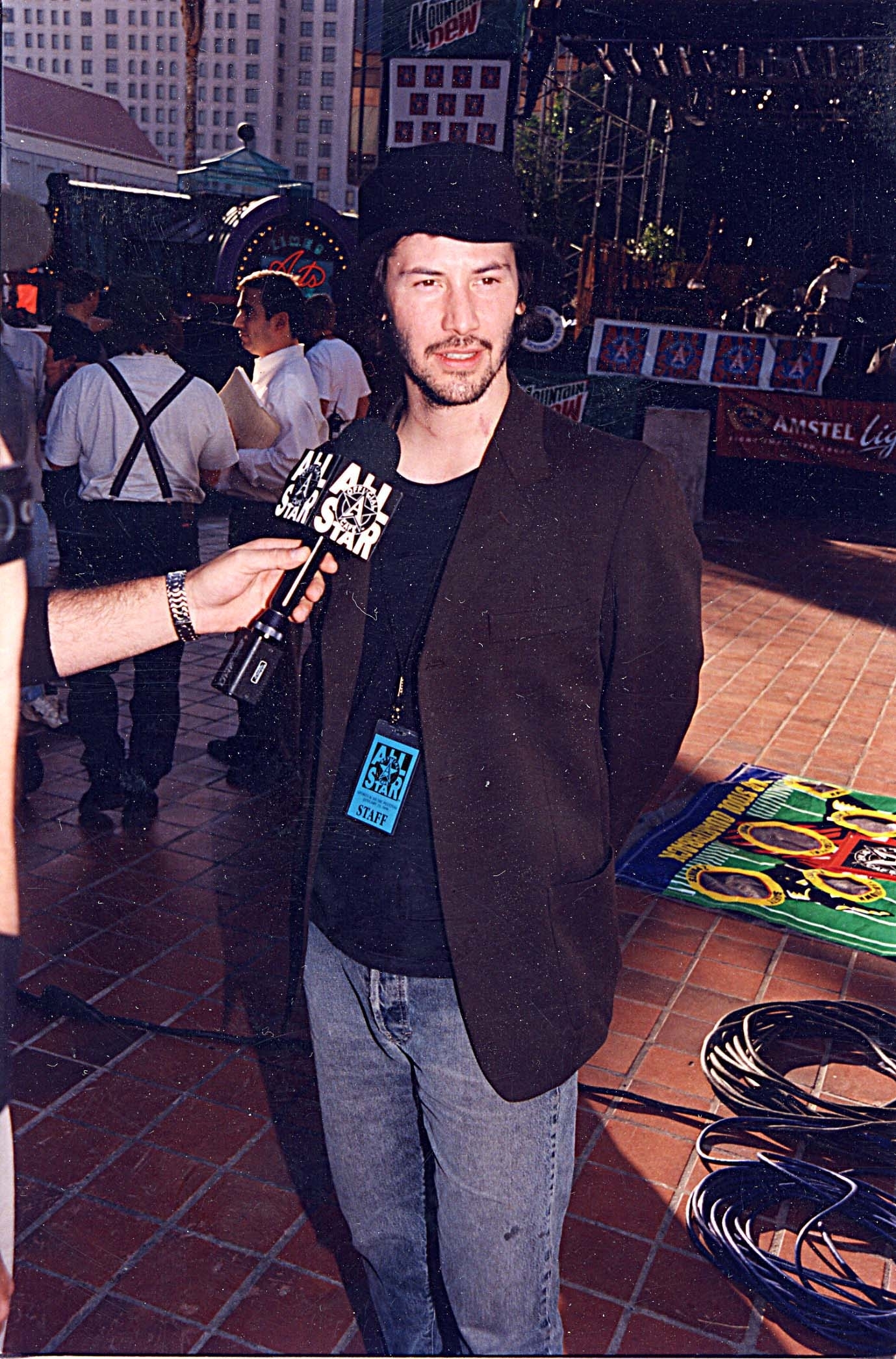 Keanu in jeans, a top, jacket, and hat, being interviewed
