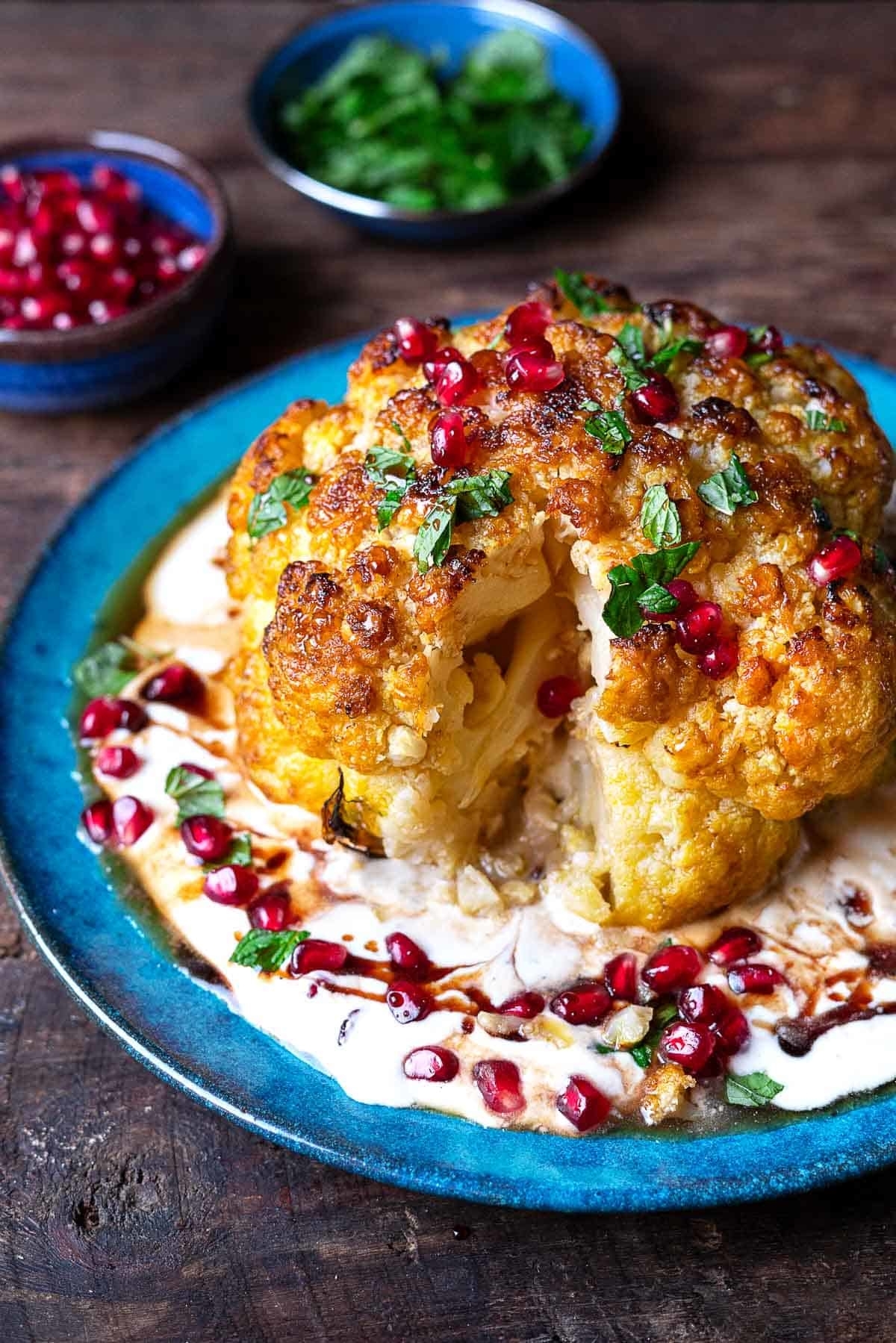 A whole cauliflower head with a slice taken out on top of whipped feta and pomegranate seeds