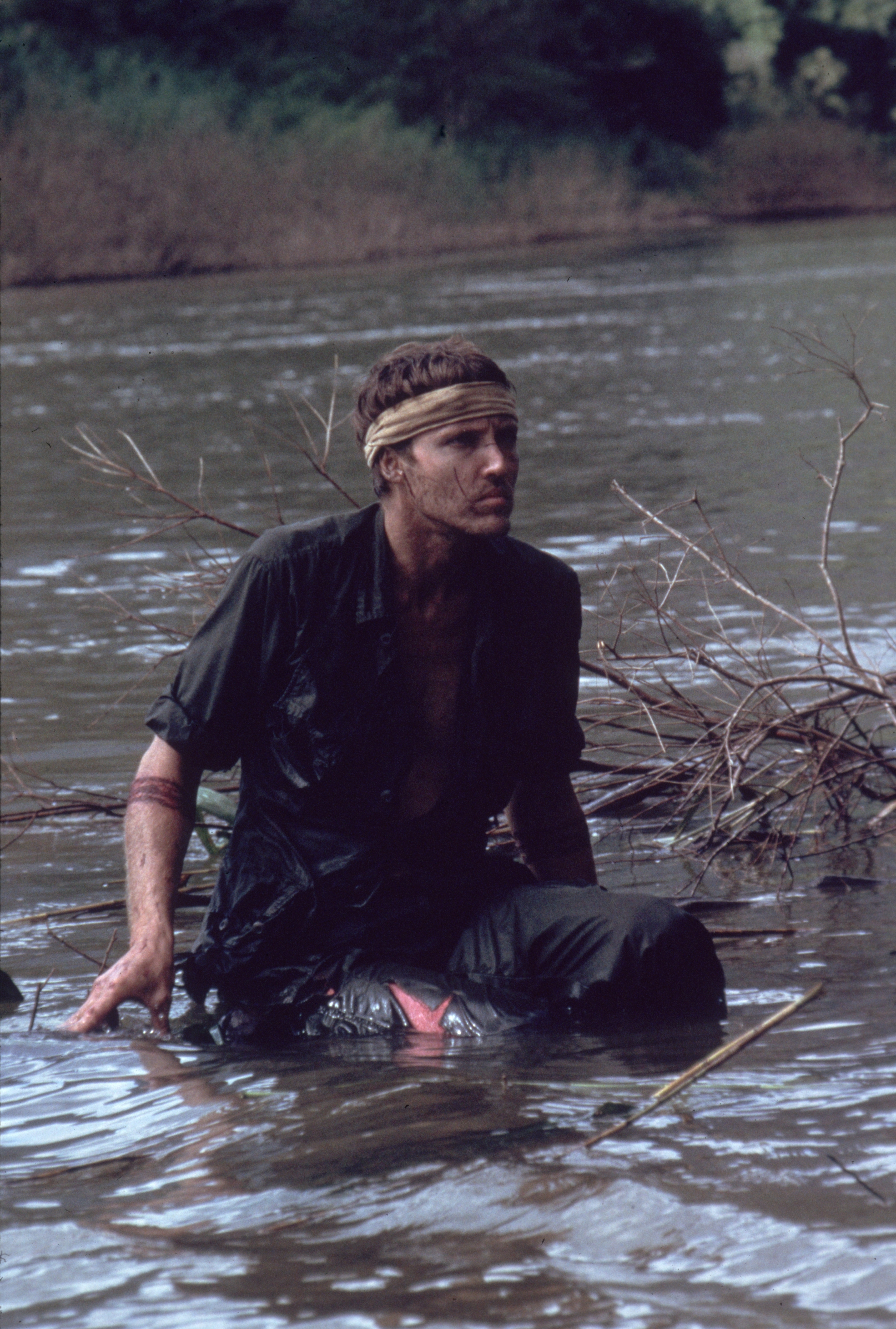 Christopher crouched in a body of water and wearing a bandana