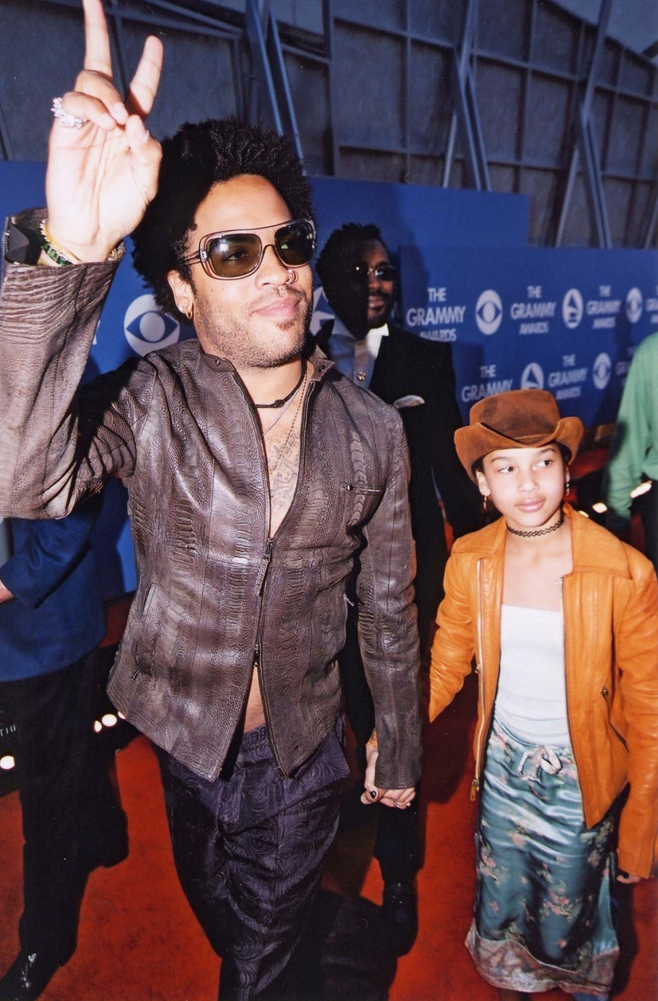 Lenny on the red carpet in an open shirt, giving the peace sign and holding the hand of his daughter, Zoë