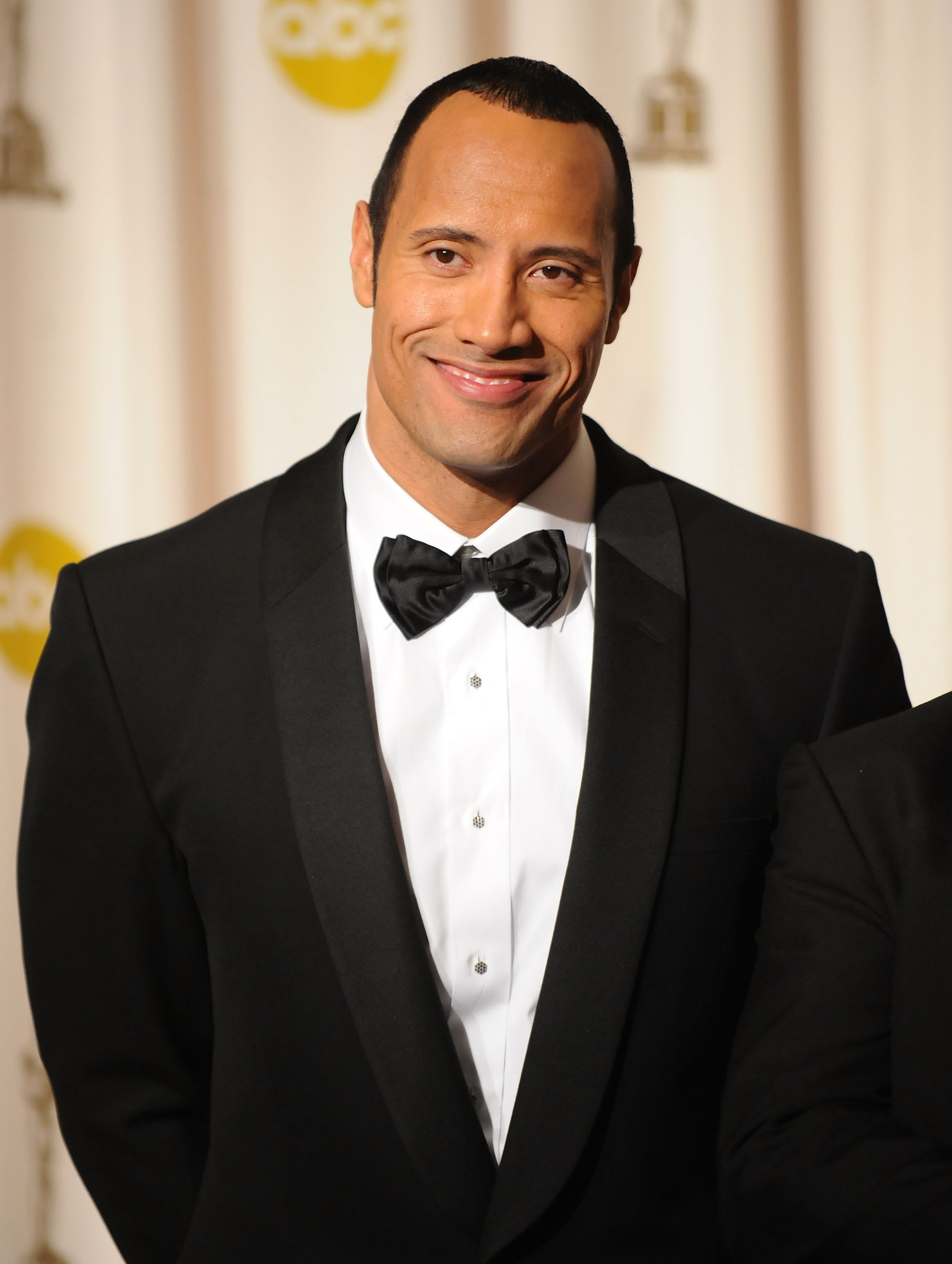 Dwayne smiling in a suit and bow tie at a media event