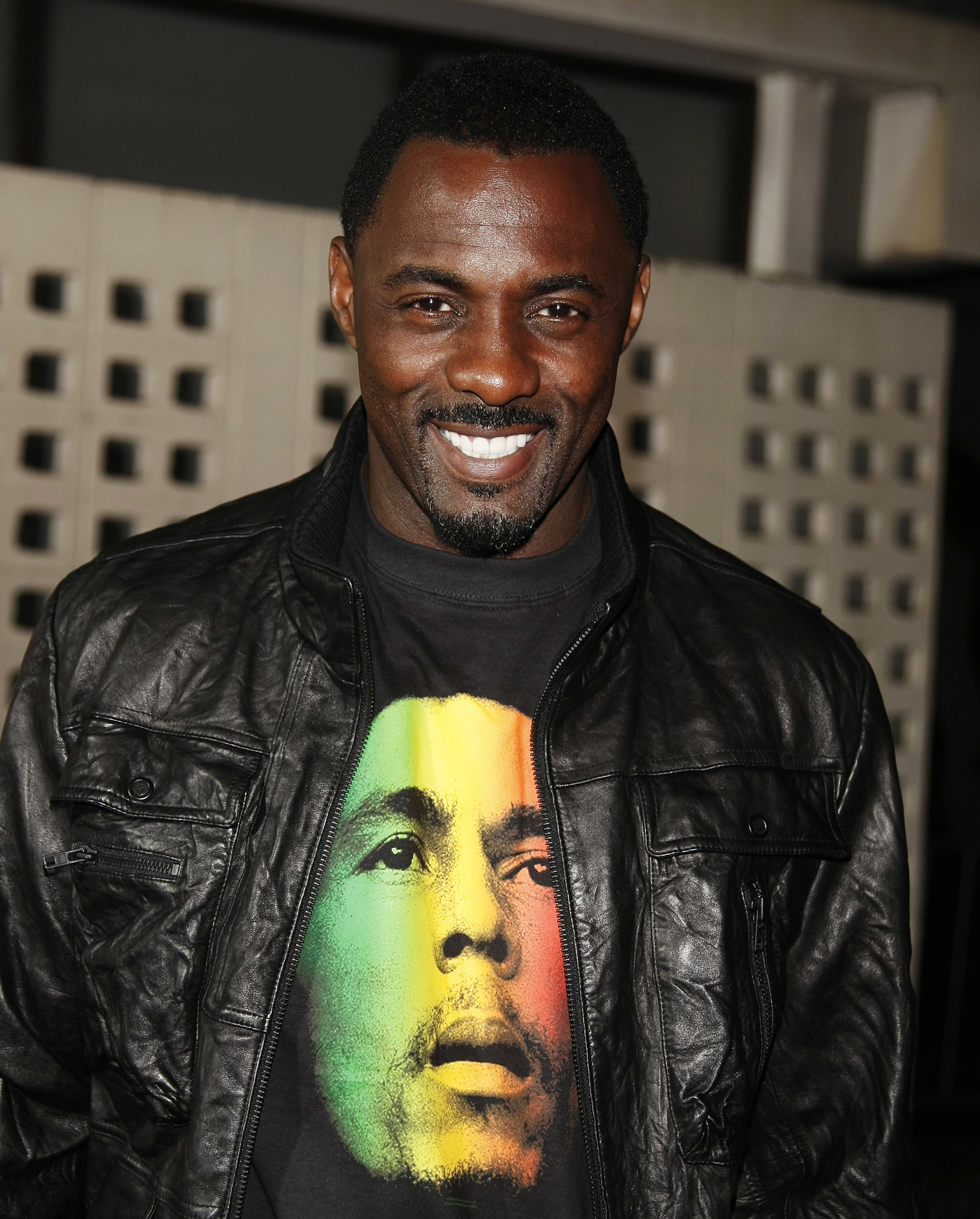 Idris smiling and wearing a leather jacket and Bob Marley T-shirt