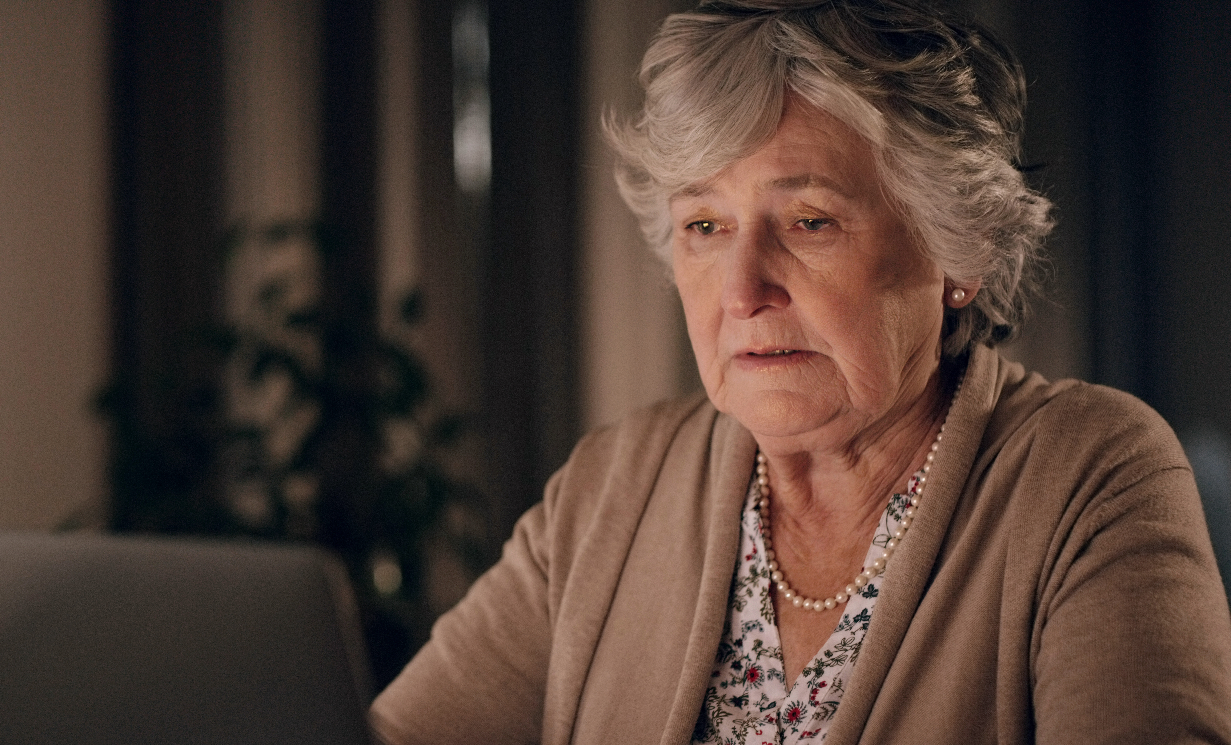 An older woman sitting in front of a laptop and looking sad