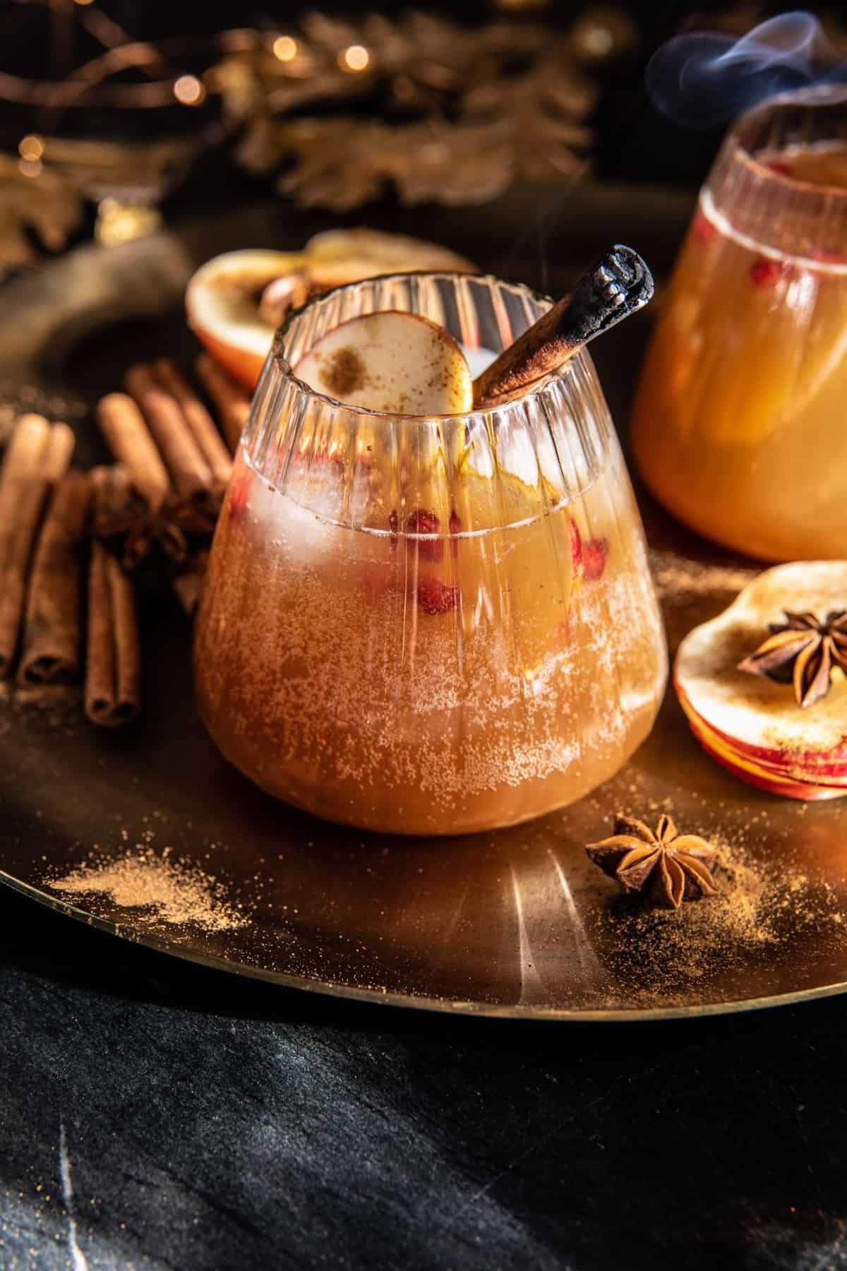 A cinnamon apple bourbon small in a glass with a smoked cinnamon stick and apple garnish